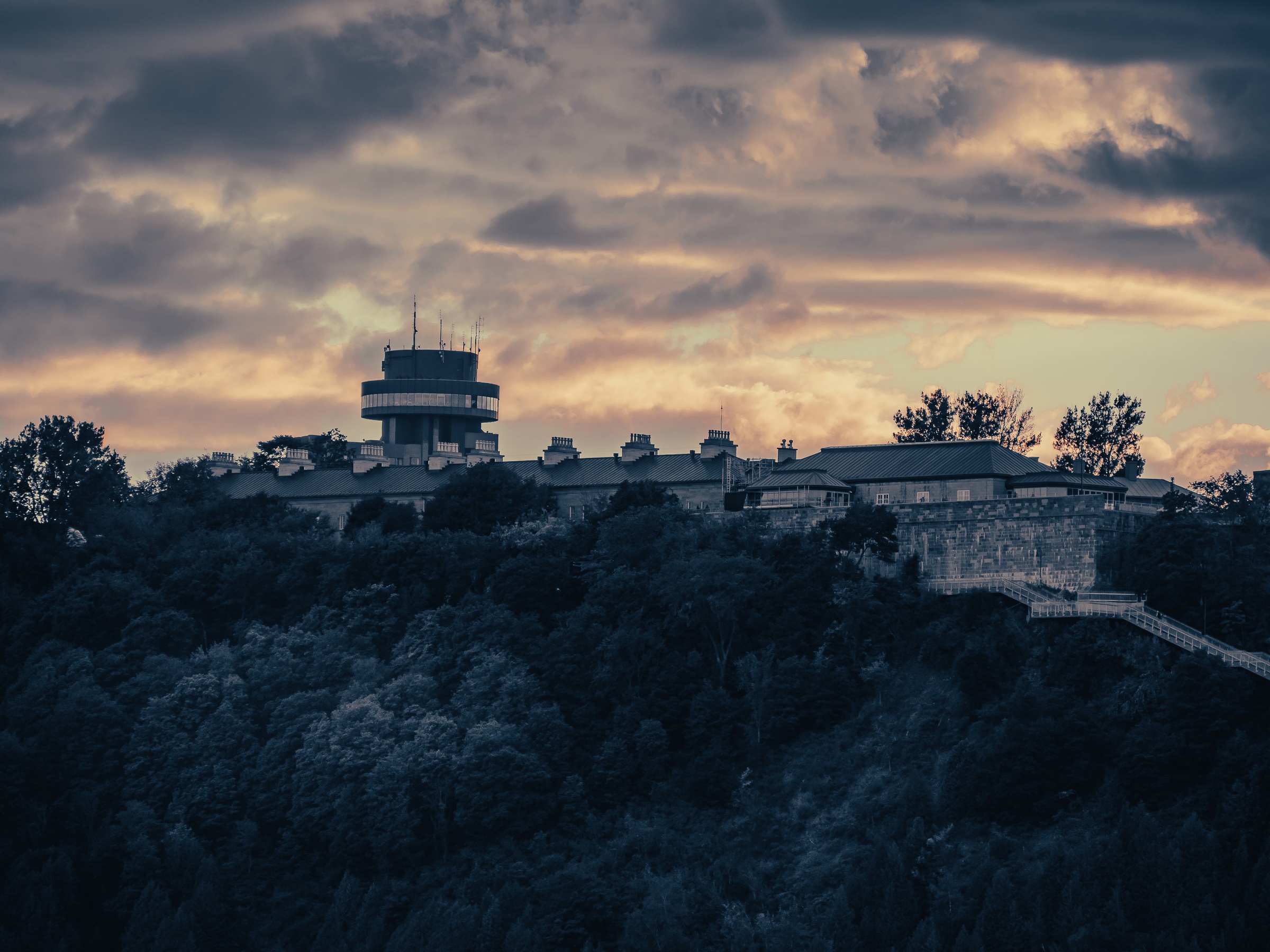 A stone building with a tower sits atop a hill, silhouetted against an orange and gray sky.