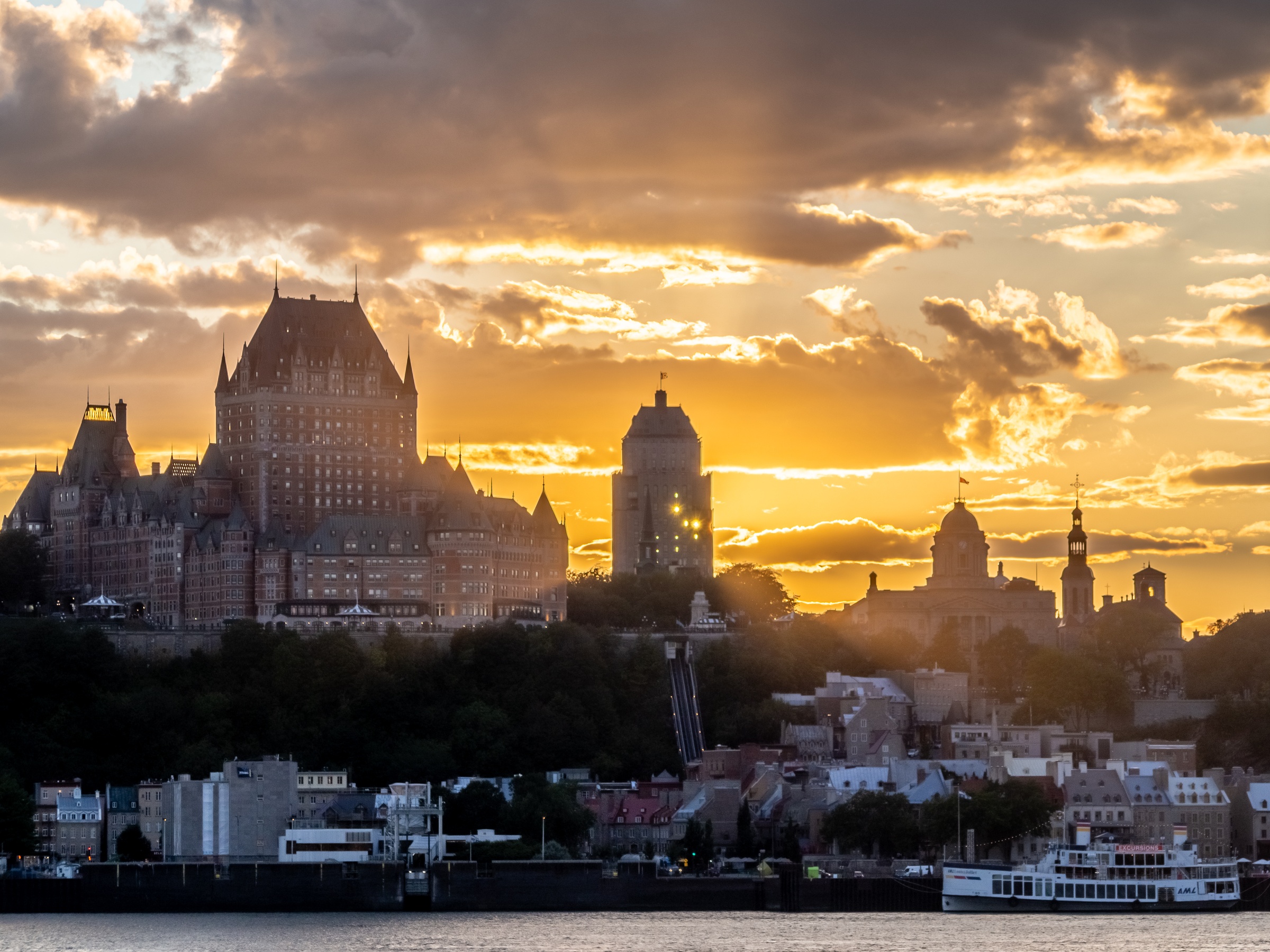 Quebec City’s Château Frontenac sits silhouetted against a vibrant sunset sky over the St. Lawrence River.