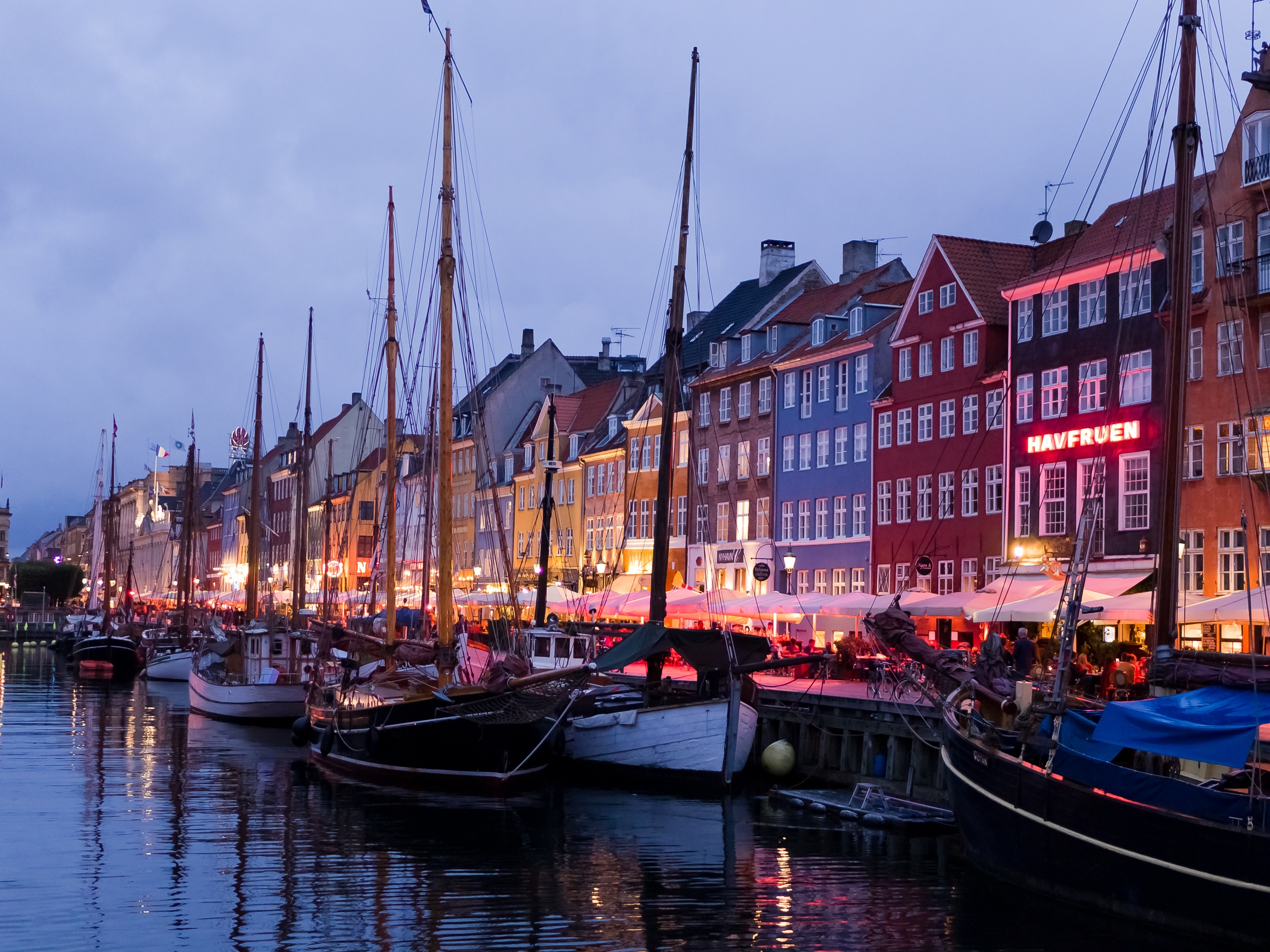 Colorful buildings and historic sailboats line a canal at twilight in Copenhagen.