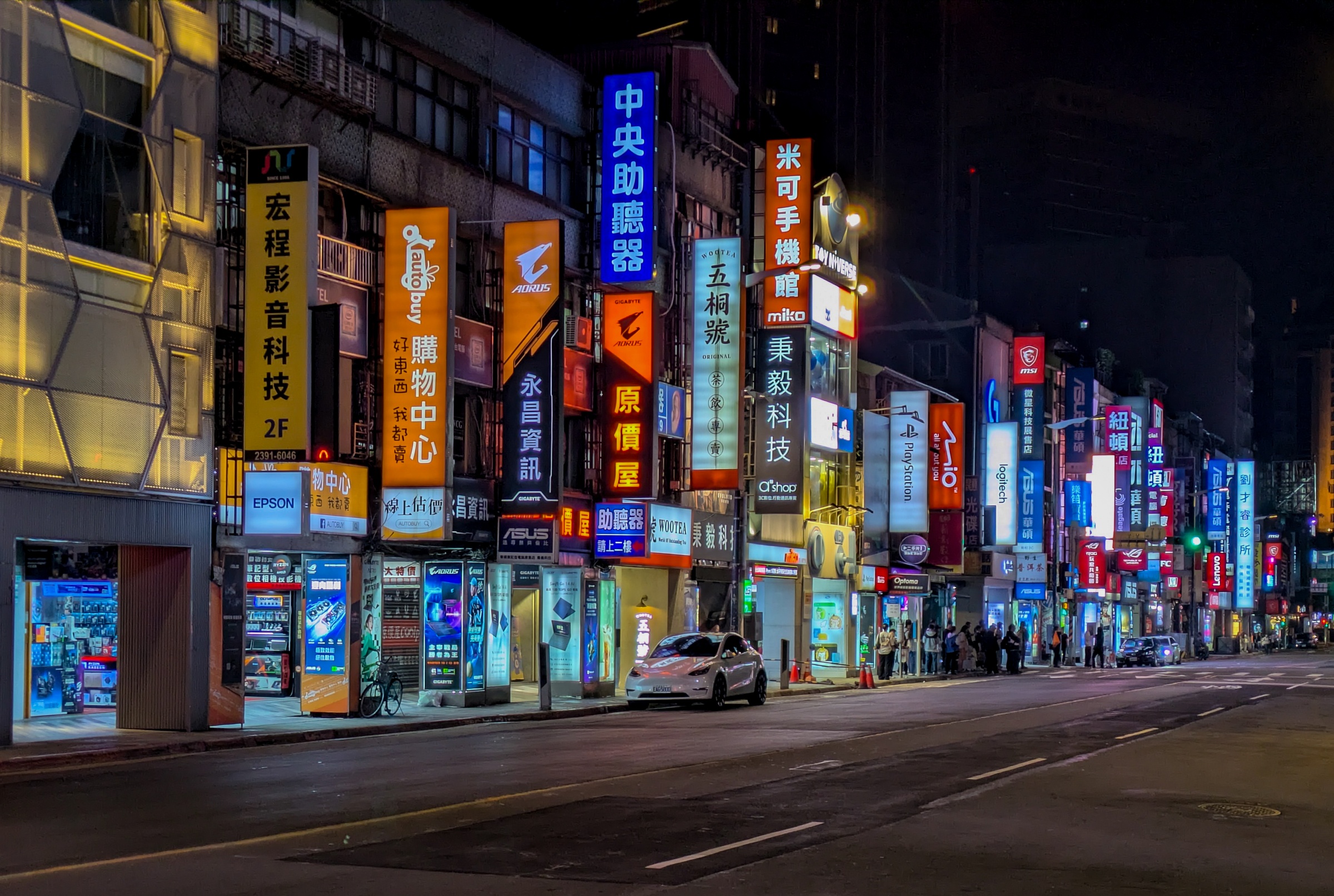 A street lined with brightly lit signs and shops stretches into the night in Taipei.
