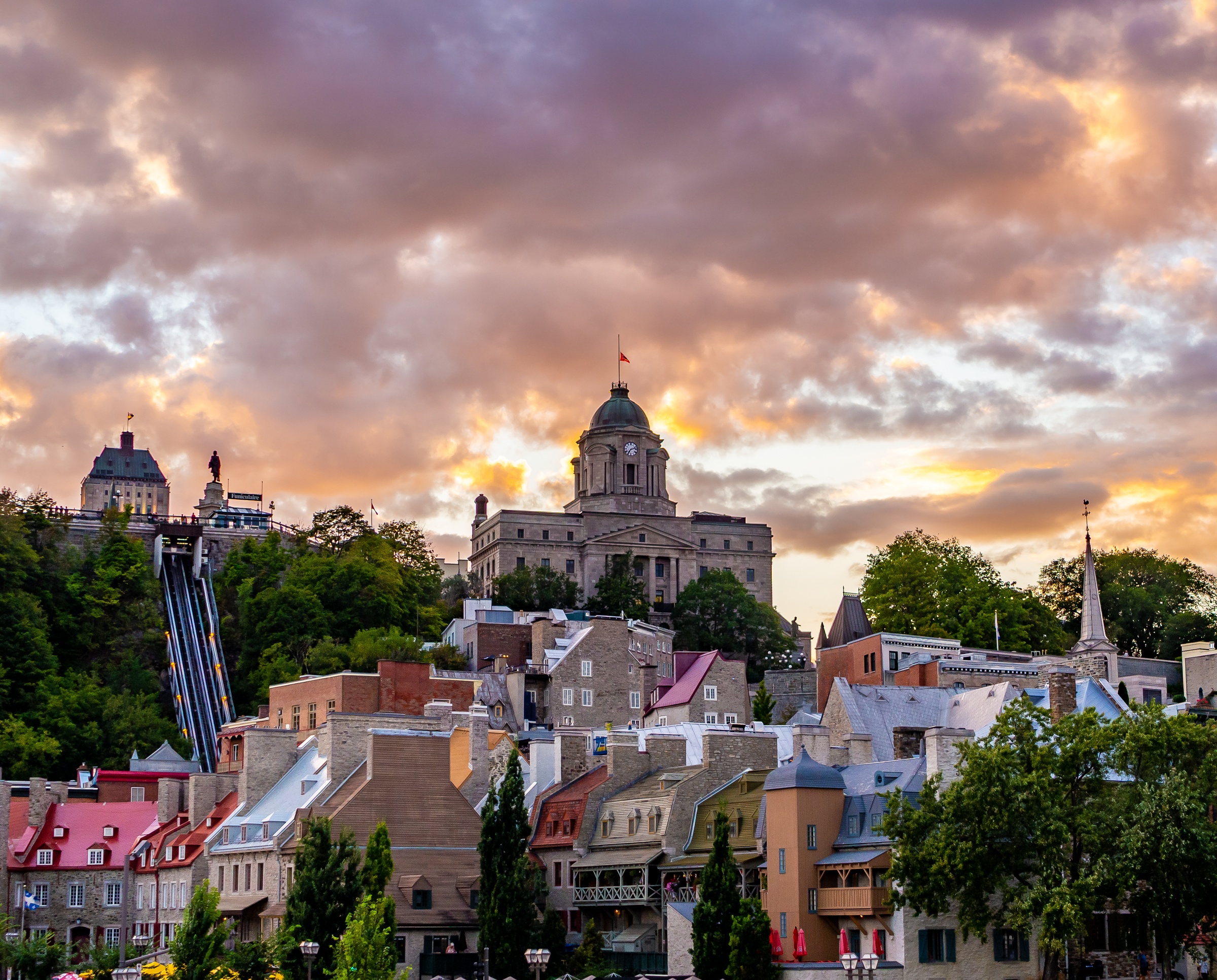 Quebec City's historic buildings and domes are framed by a vibrant sunset sky.