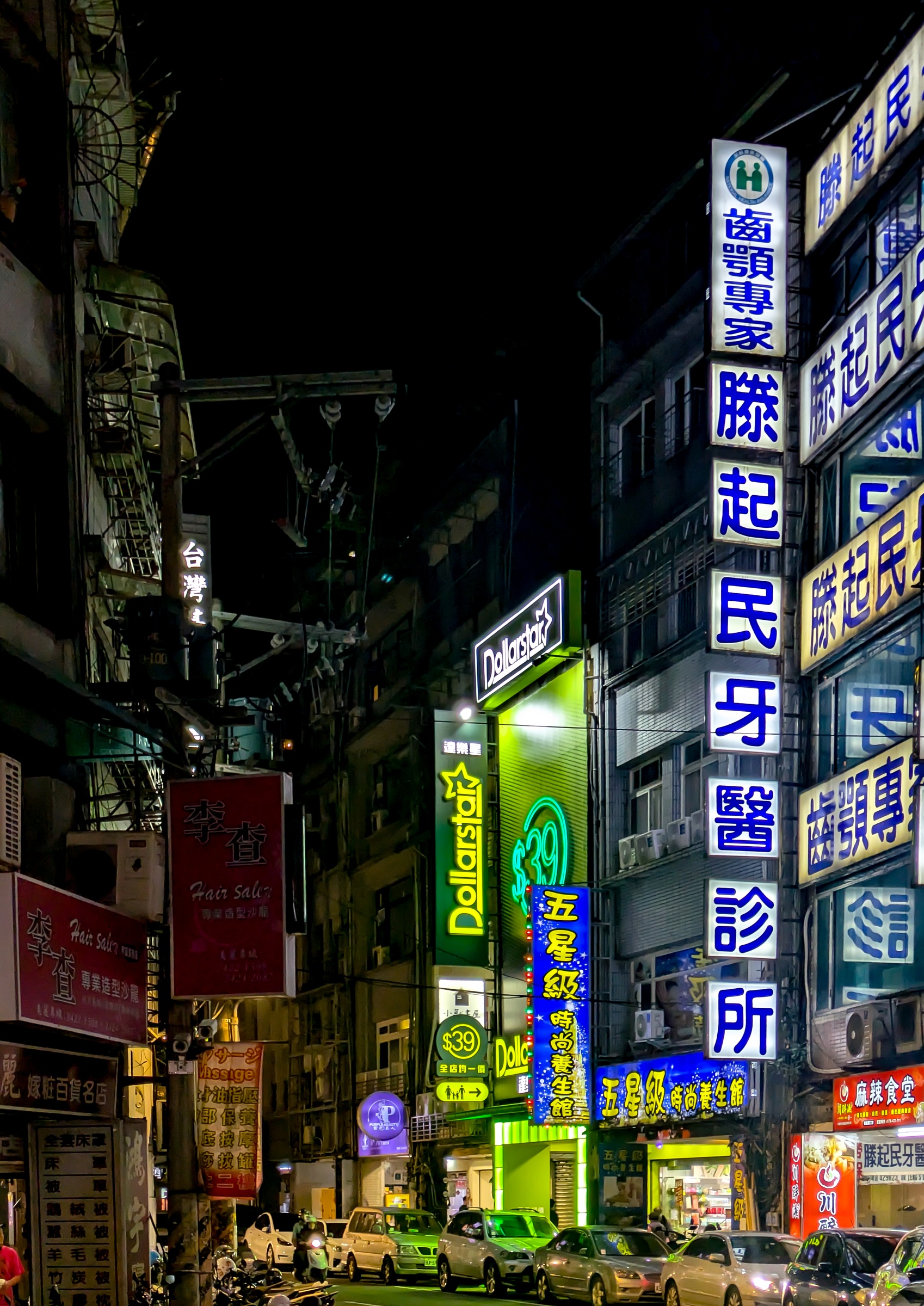 Neon signs illuminate a narrow street lined with buildings in a bustling Asian city at night.