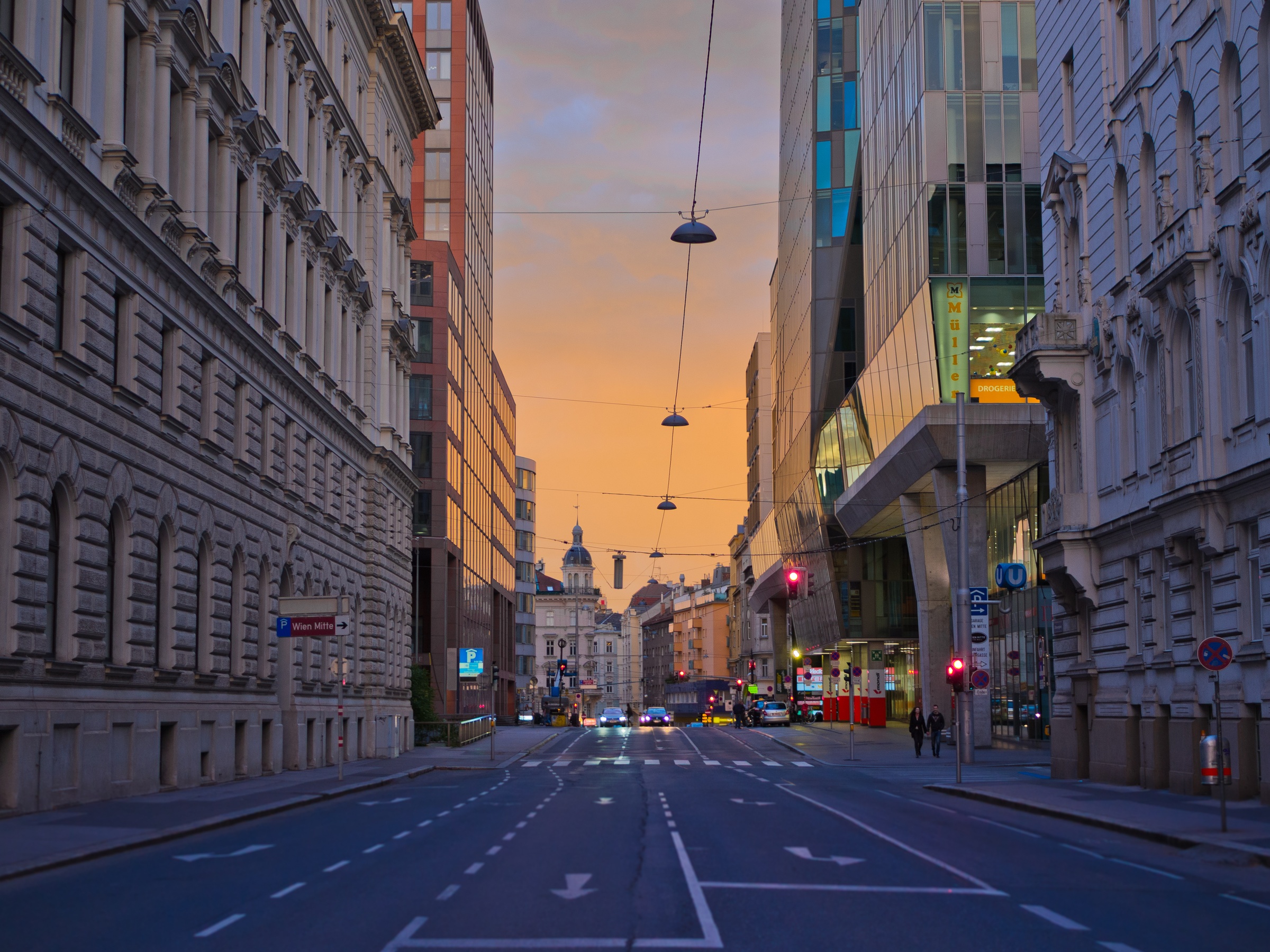 A long, empty street stretches between historic buildings and modern architecture at dusk in Vienna.