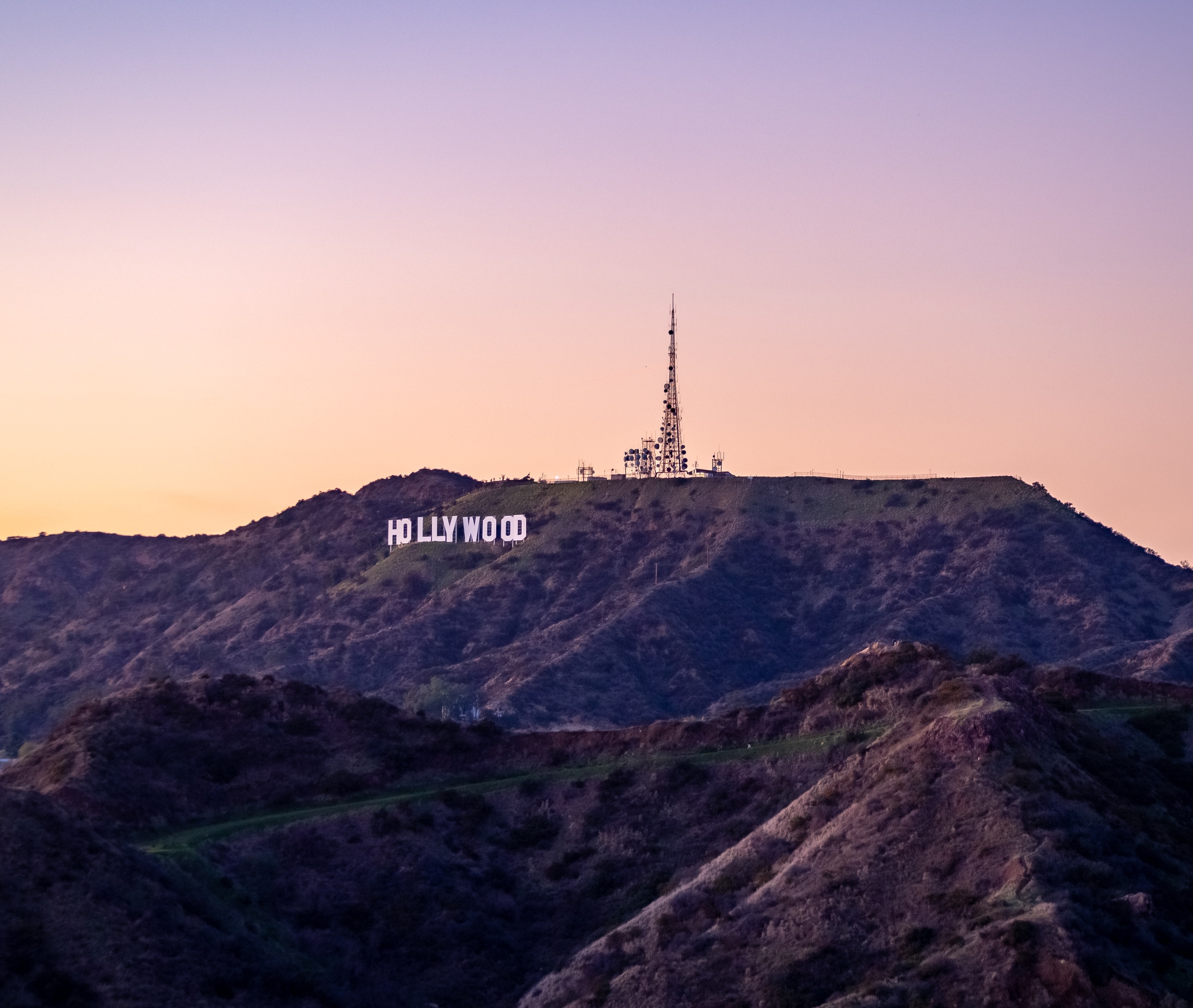 The Hollywood Sign sits atop a hillside against a soft, colorful sunset sky.