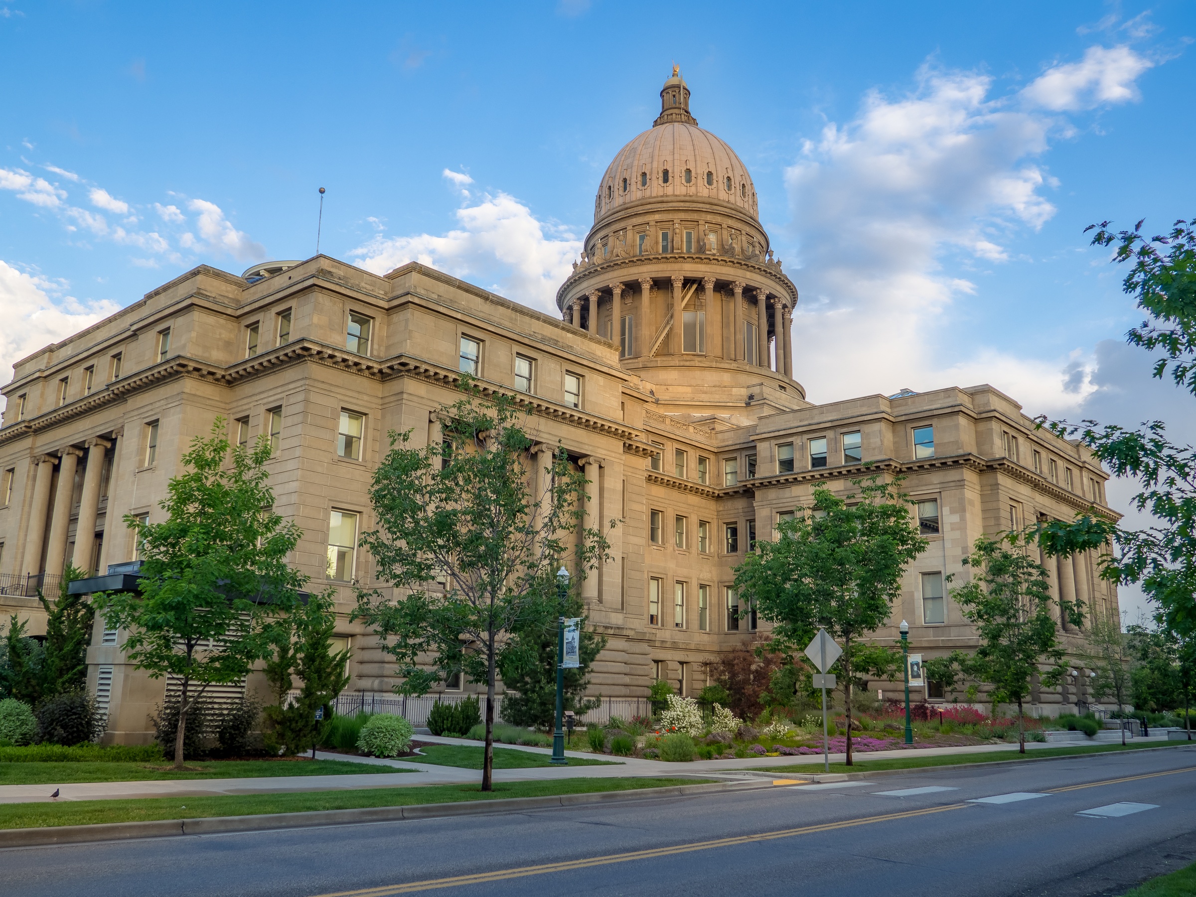 The Idaho State Capitol building stands tall against a partly cloudy blue sky.