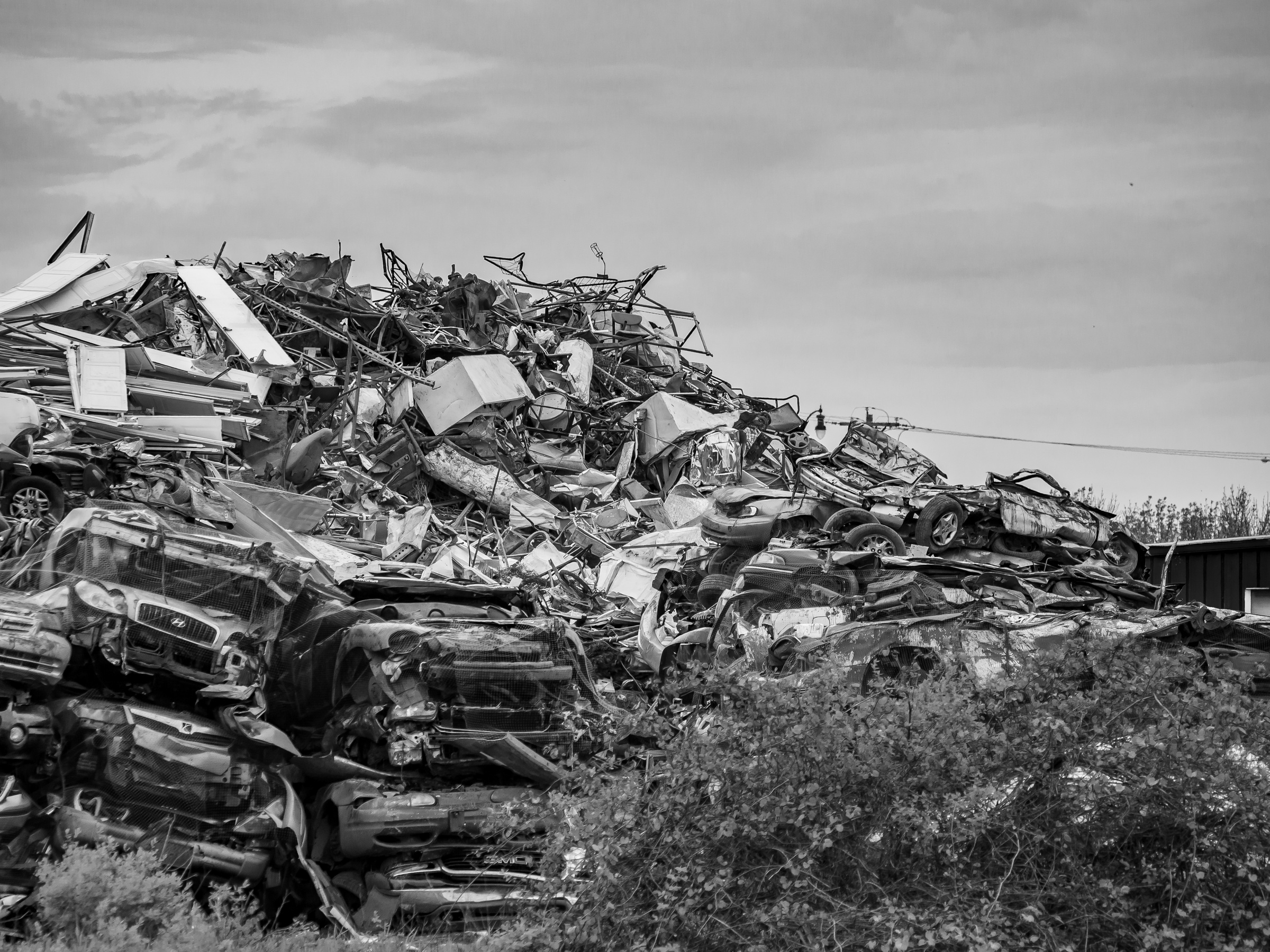 A large pile of crushed and discarded cars sits on a hillside under an overcast sky.