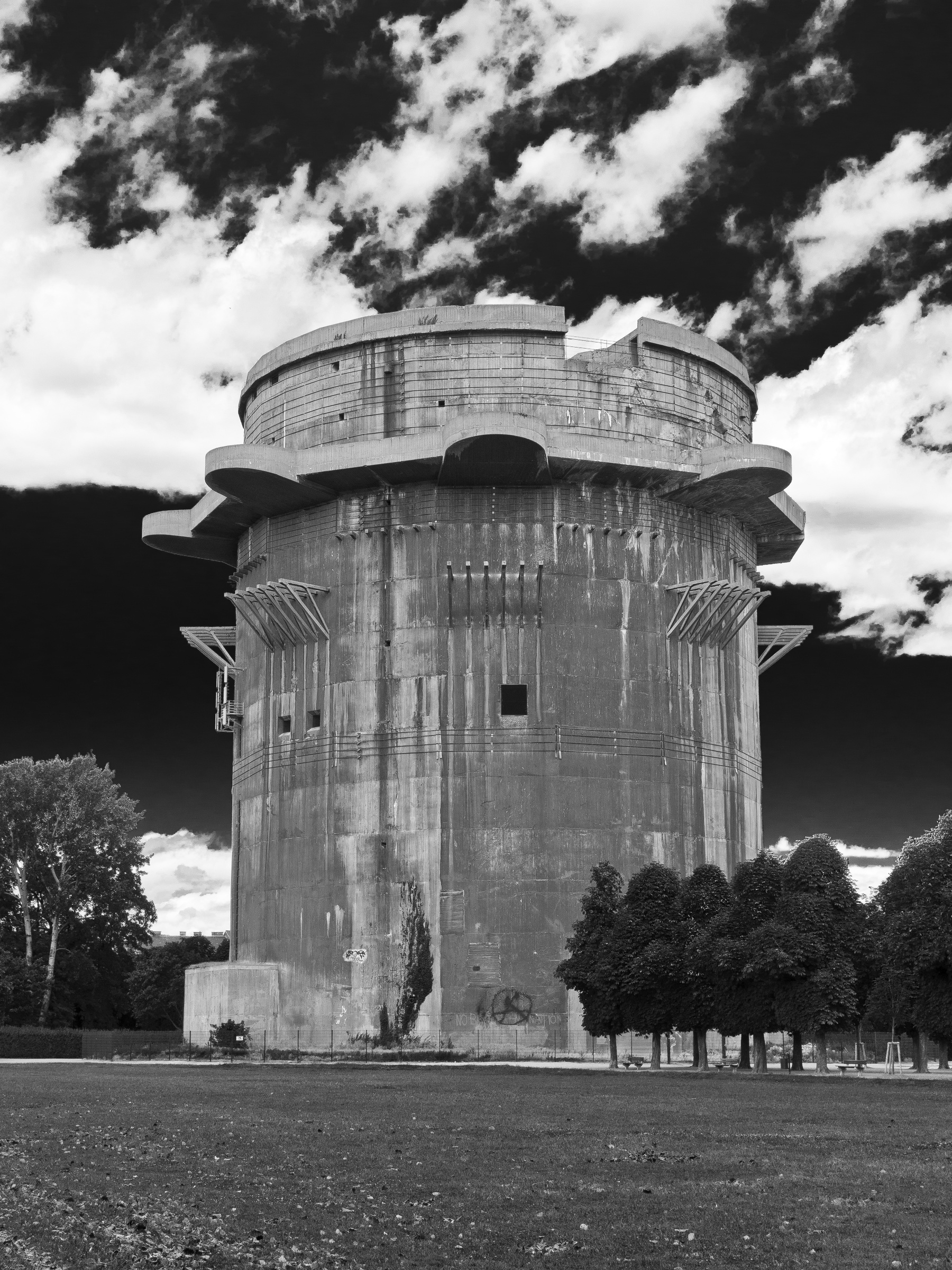 A concrete anti-aircraft tower stands in a grassy field beneath a cloudy sky.