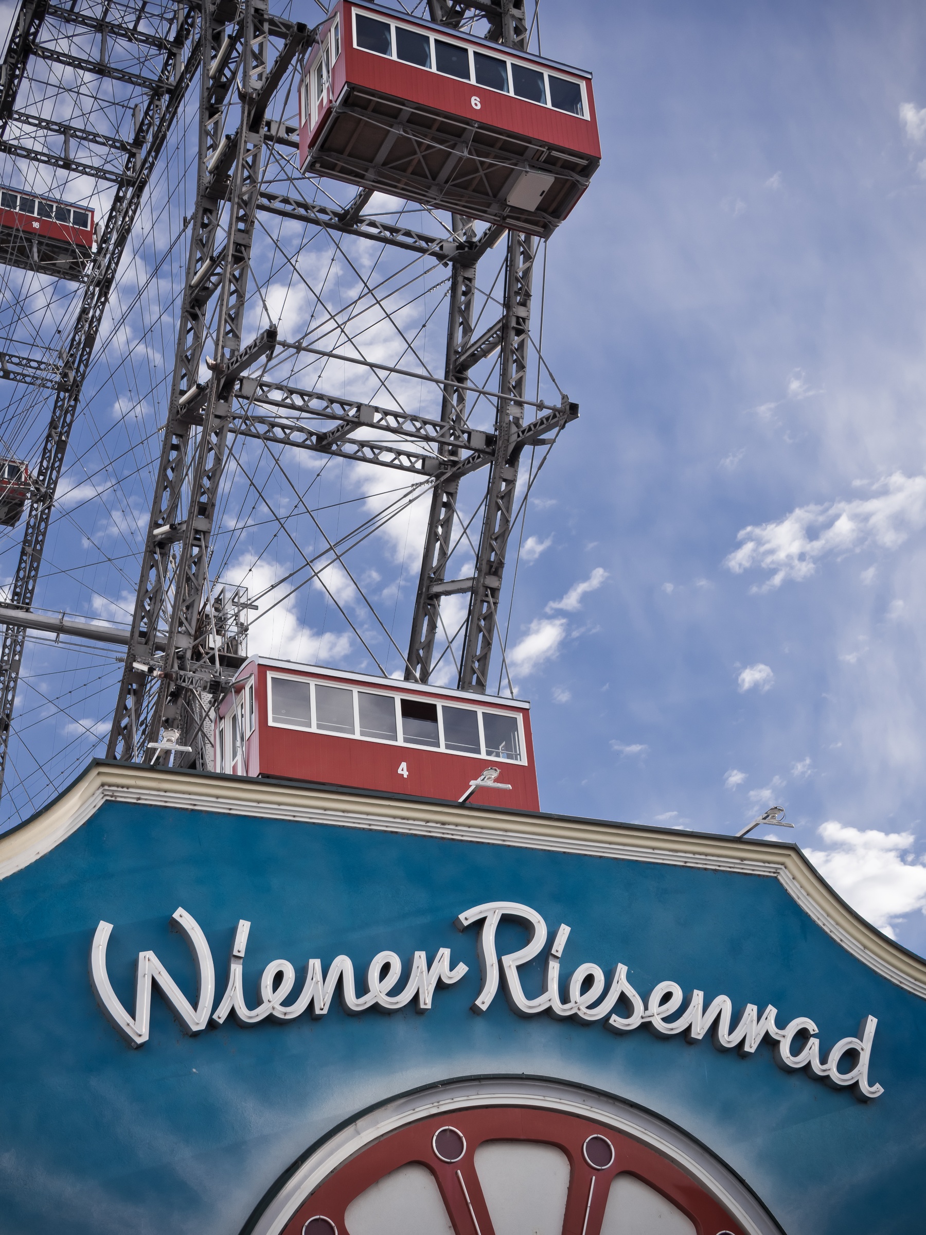 The Wiener Riesenrad Ferris wheel rises against a blue sky above its turquoise entrance sign.