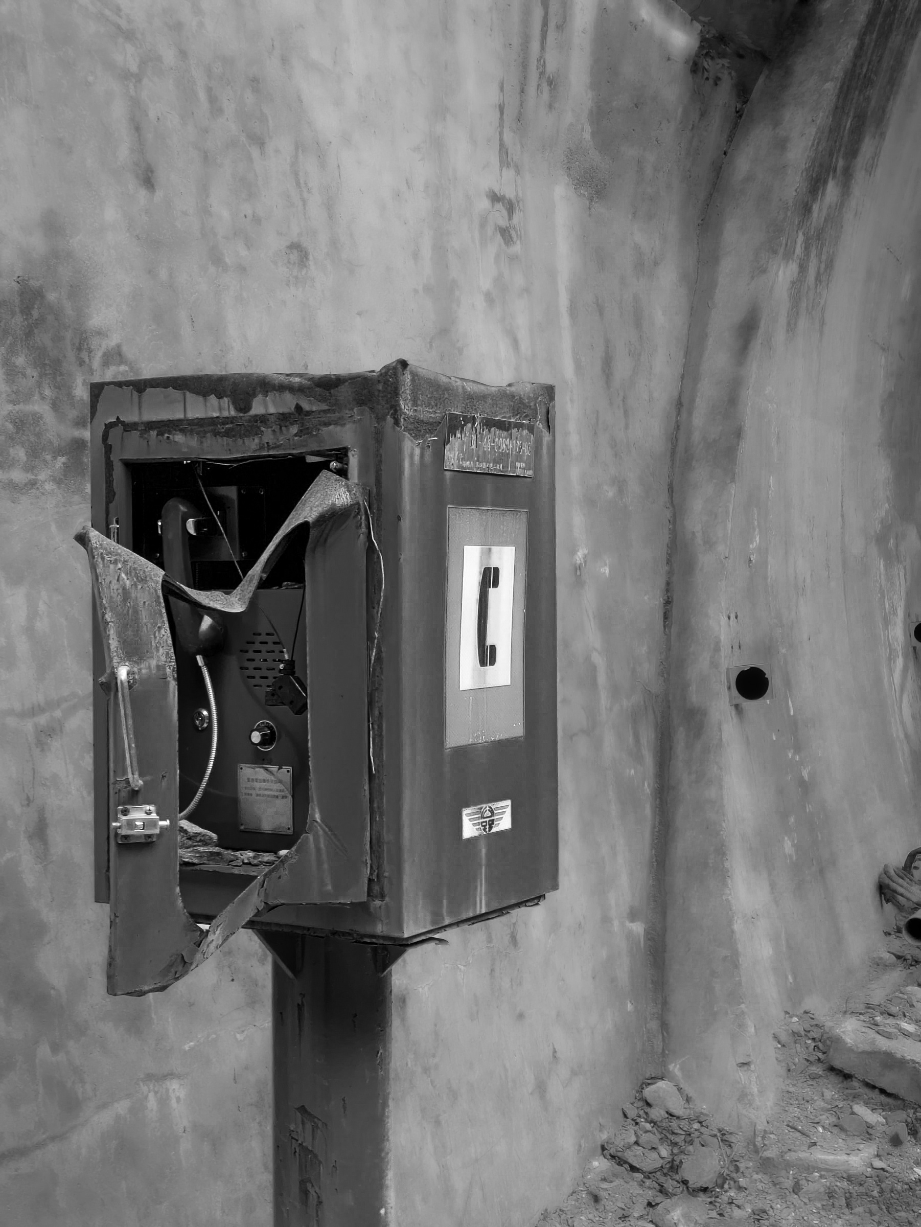 A weathered public telephone sits within a curved, concrete tunnel wall.