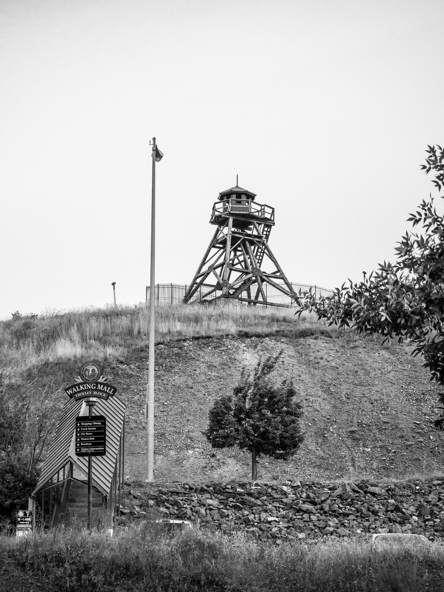 A historic fire lookout tower sits atop a hill overlooking a sign and grassy landscape.