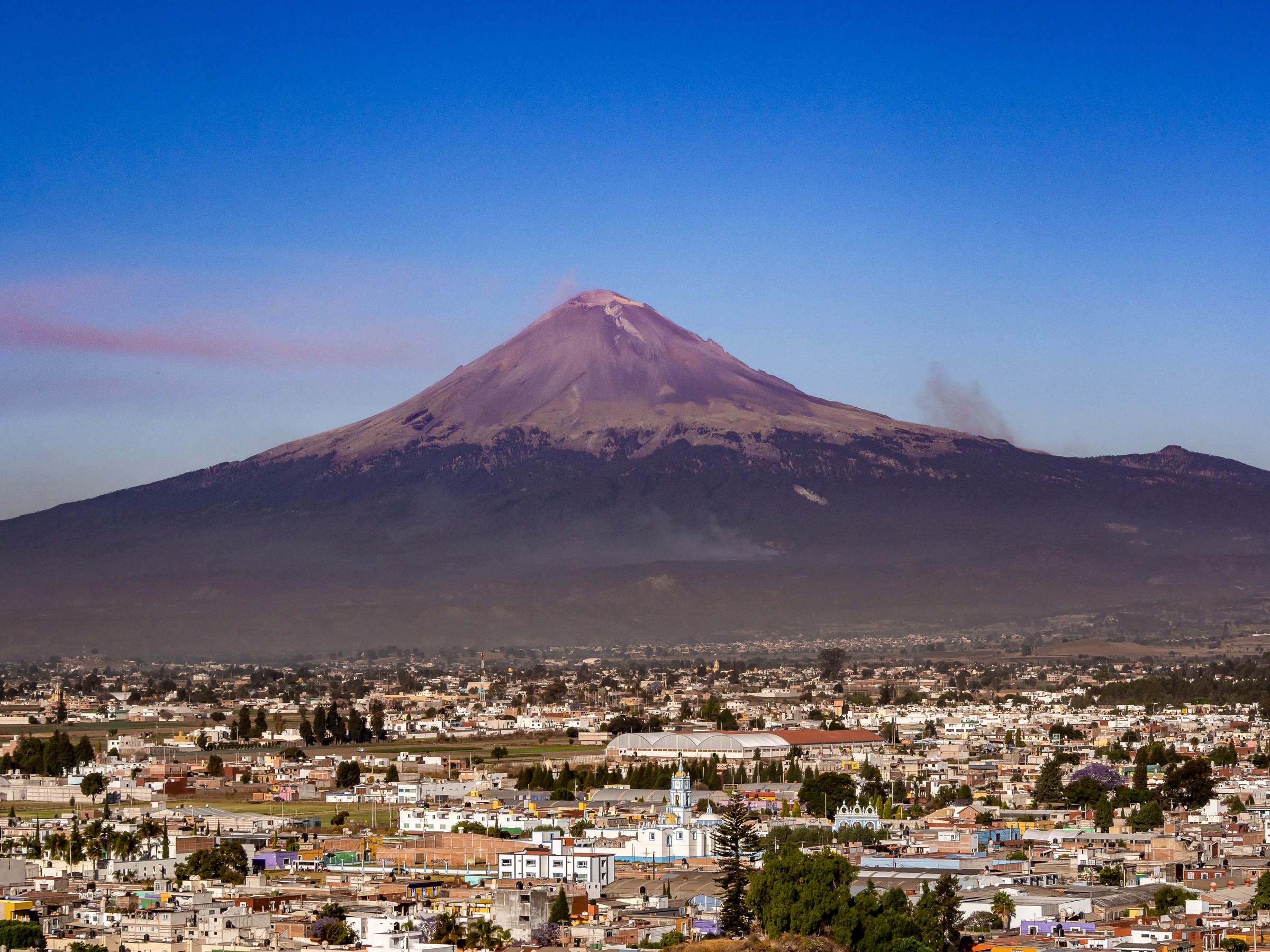 A large volcano towers over a sprawling town beneath a clear blue sky.
