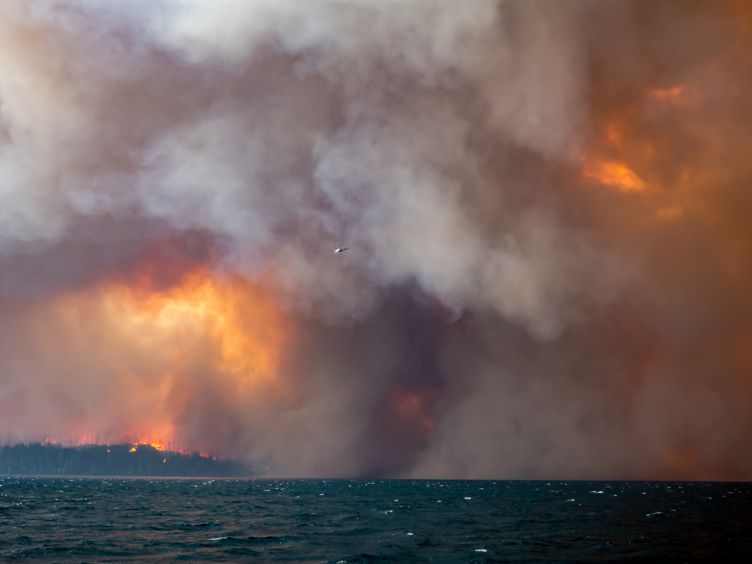 Thick smoke and orange flames rise above a dark body of water.