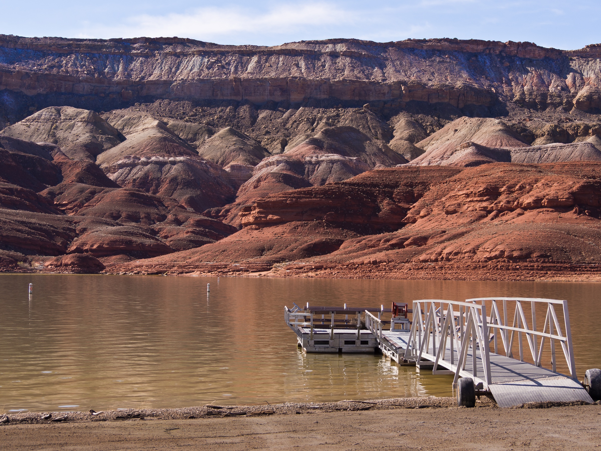 A metal dock extends into a lake before towering red rock cliffs.