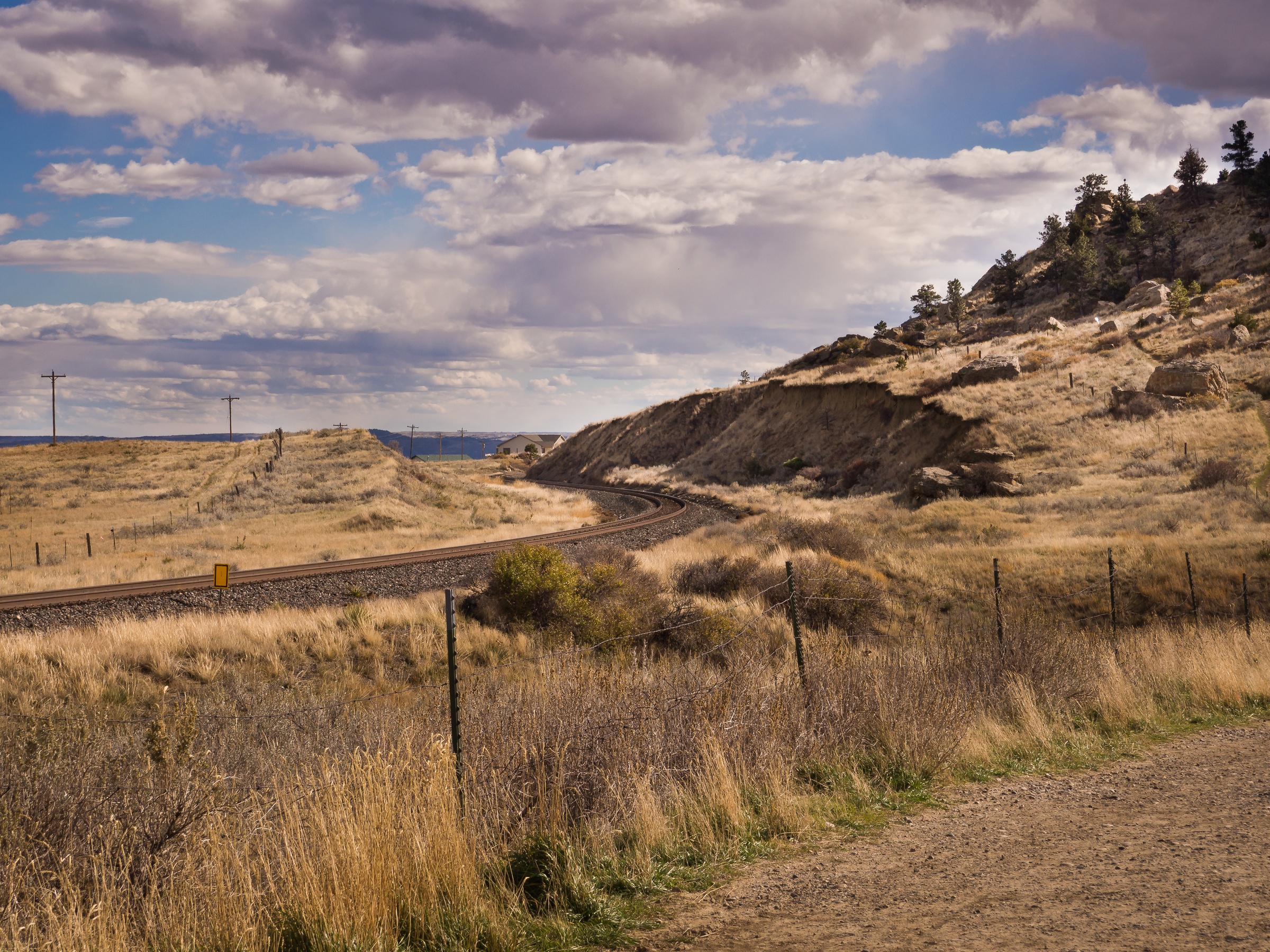 A railway track curves through a dry, hilly landscape under a cloudy sky.