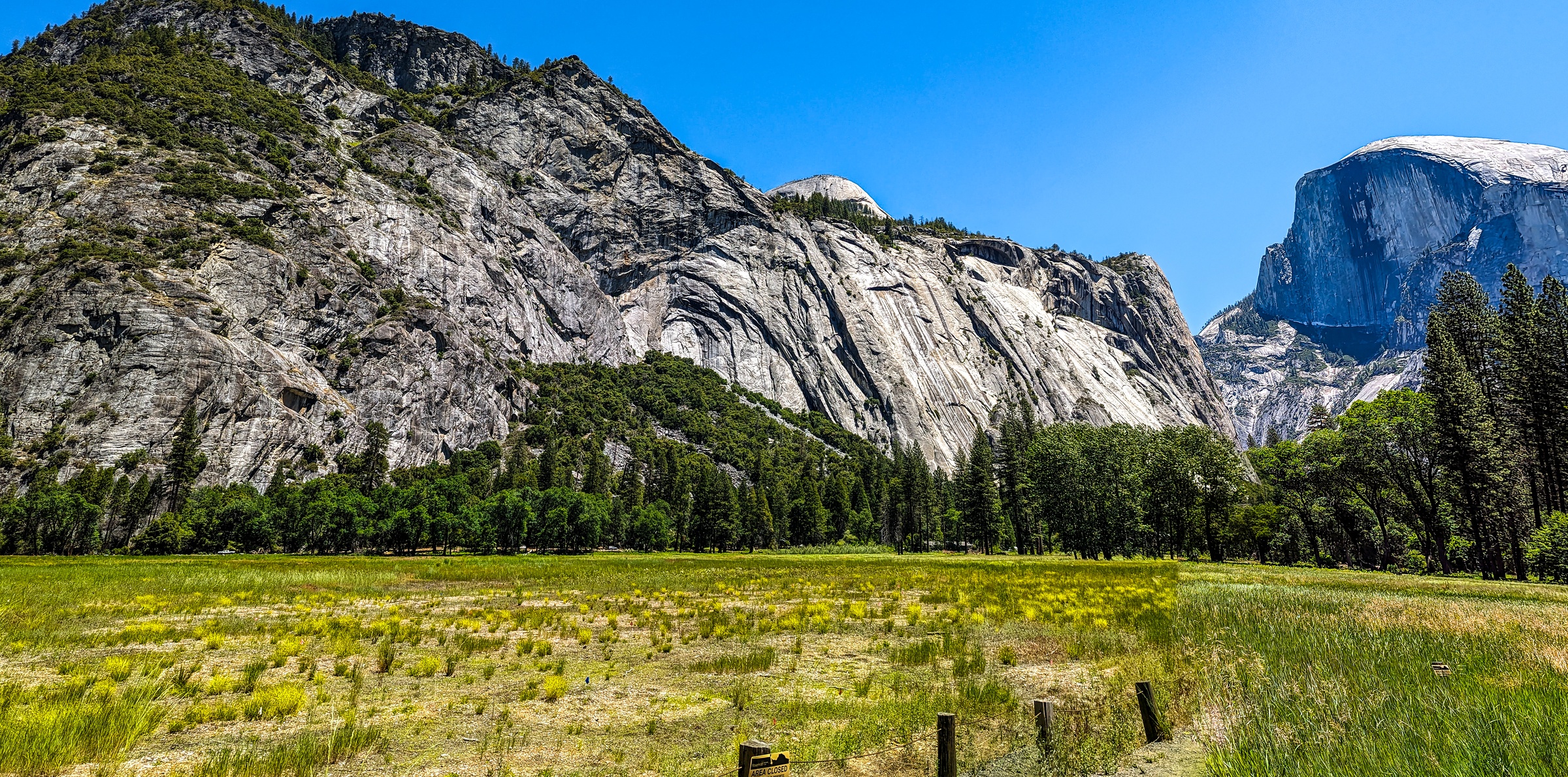 Massive granite cliffs tower over a green meadow under a clear blue sky.