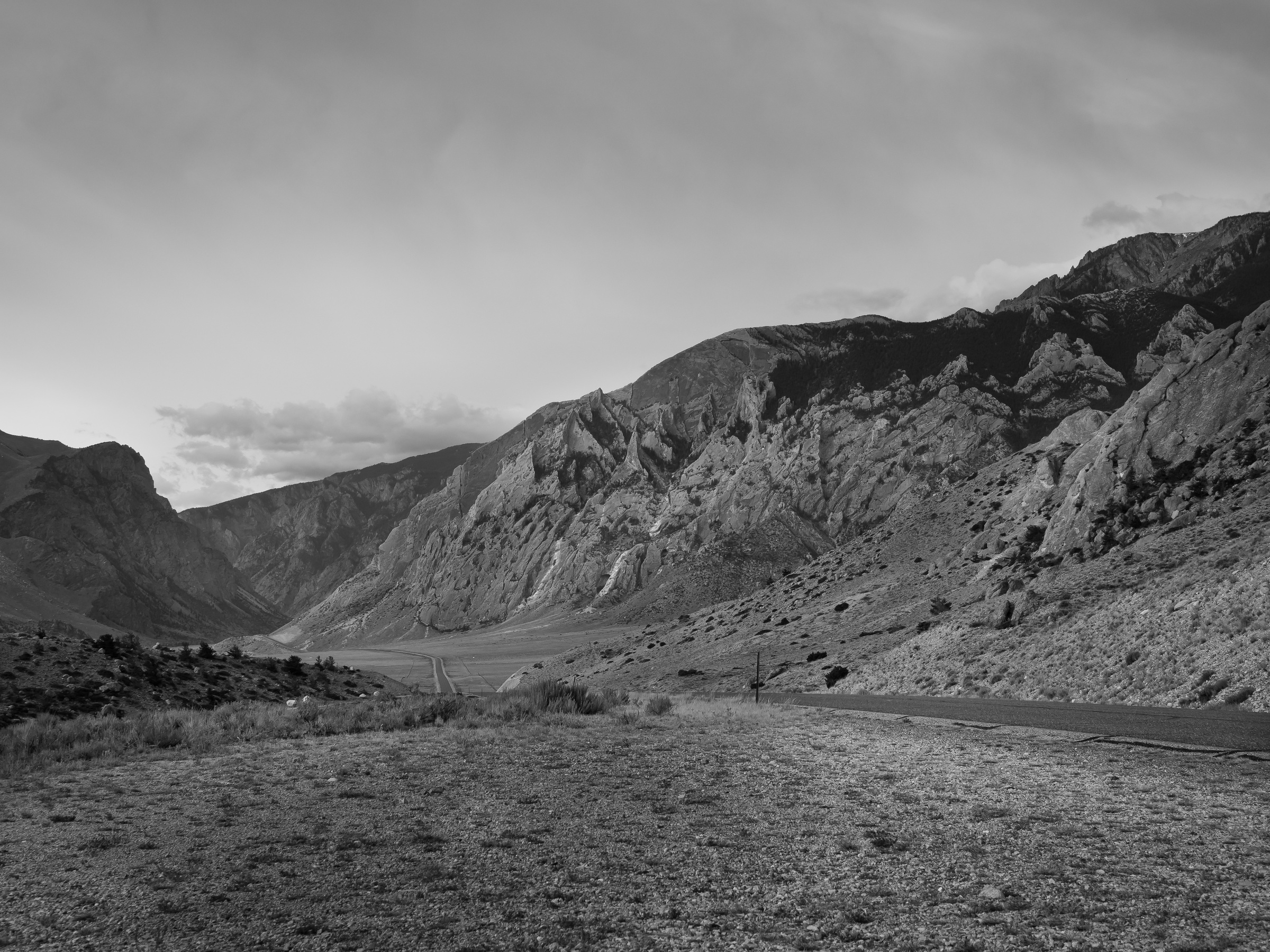 A road winds through a rugged mountain valley beneath an overcast sky.