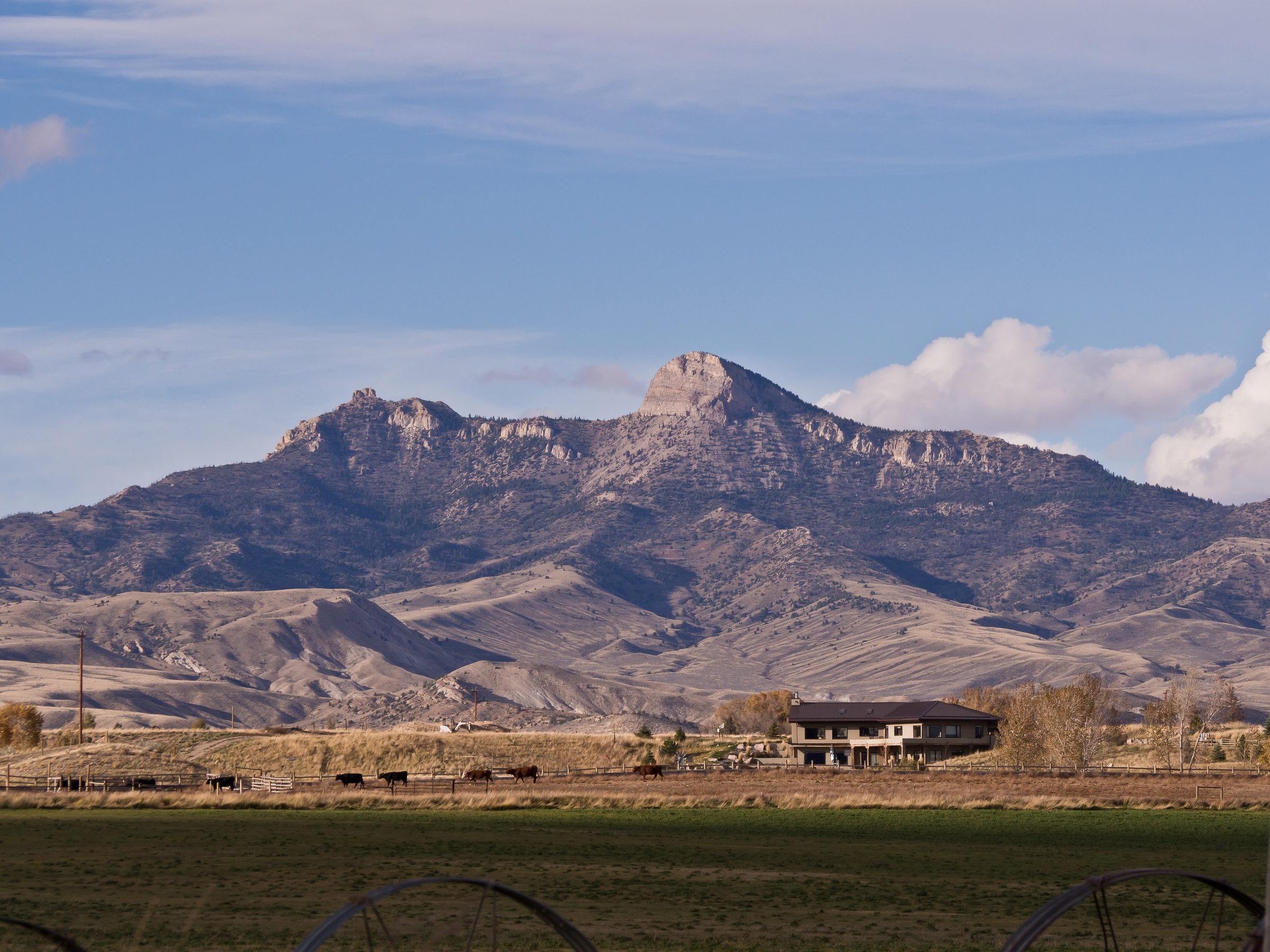A large rocky mountain towers over rolling hills and a house in a rural landscape.