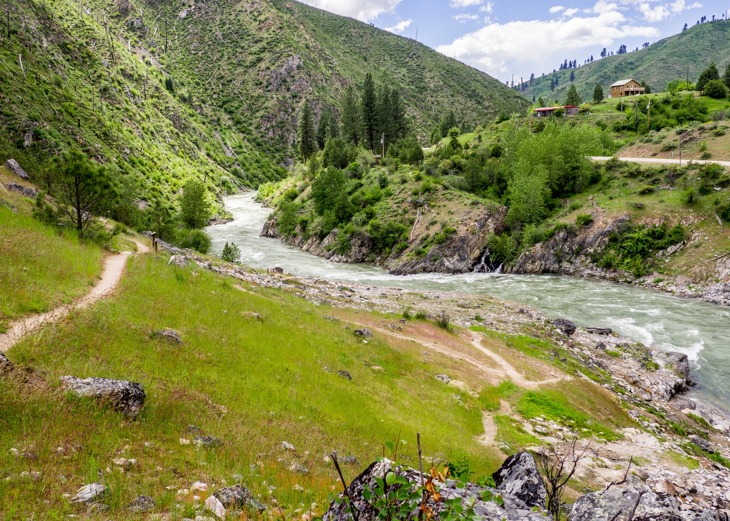 A rushing river winds through a green mountain valley with small buildings on the slopes.