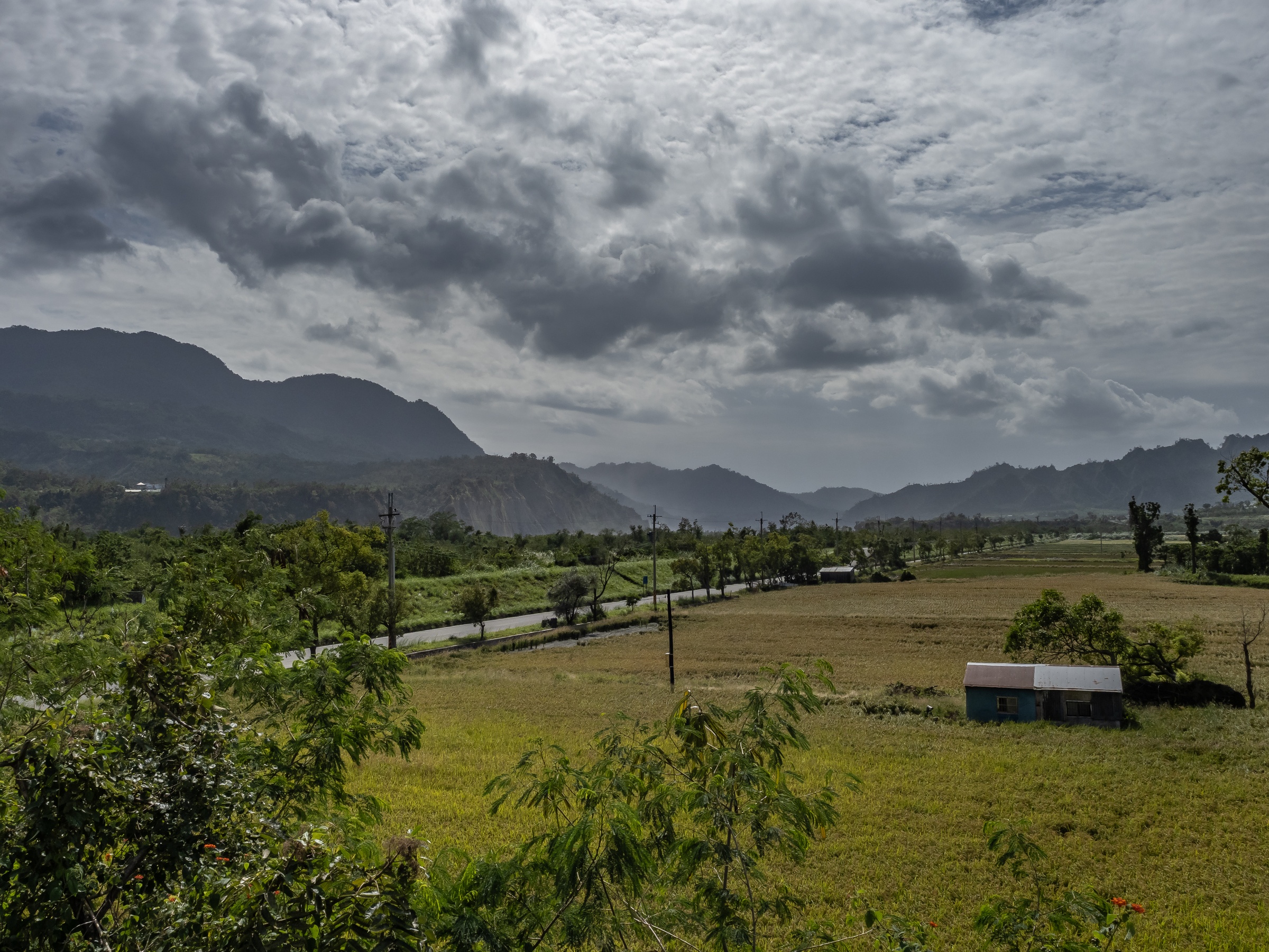 A small blue building sits in a grassy field beneath distant mountains and a cloudy sky.