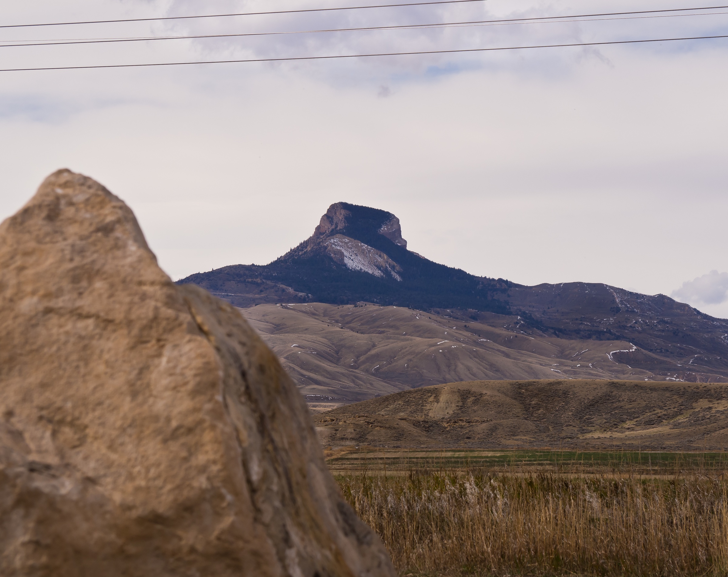 A flat-topped mountain rises above rolling brown hills and a large rock.