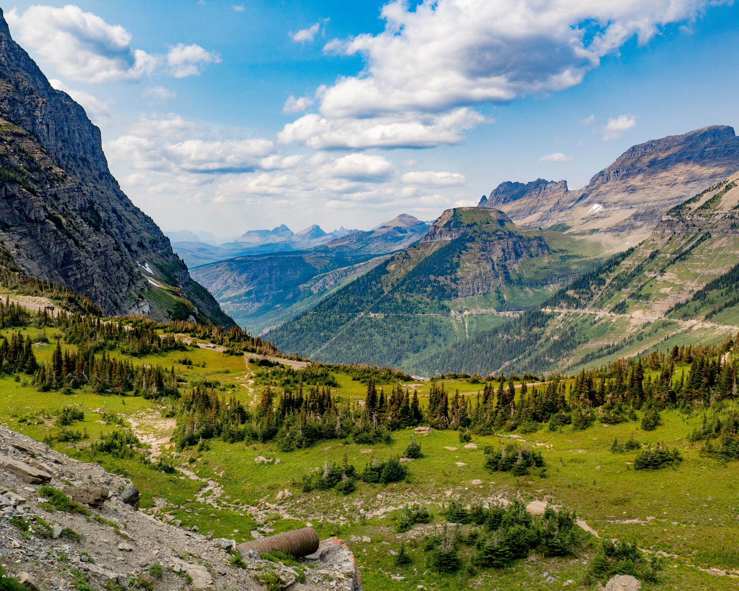 A lush green mountain valley surrounded by rugged peaks under a cloudy blue sky.