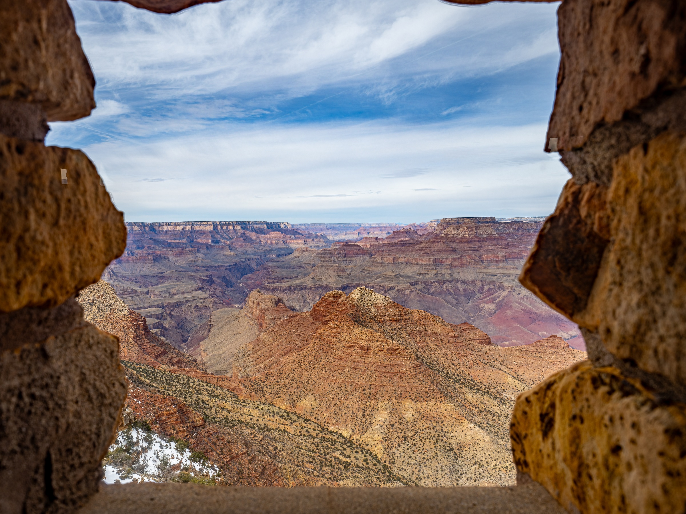 The Grand Canyon viewed through a rough stone window frame.