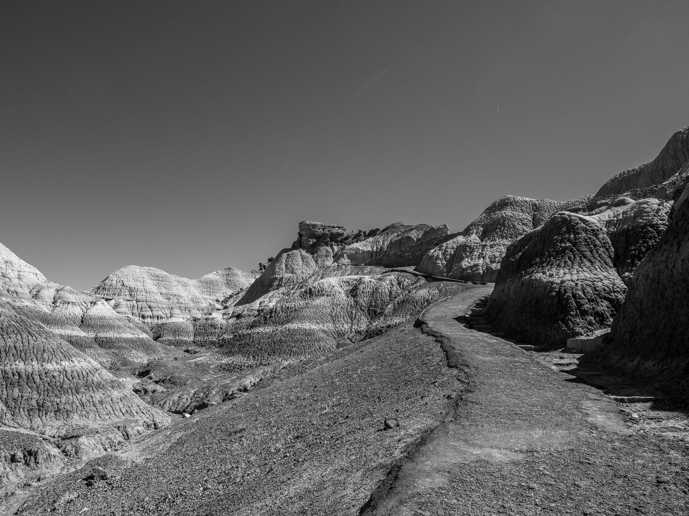 A winding dirt path leads through a valley of striped rock formations under a clear sky.