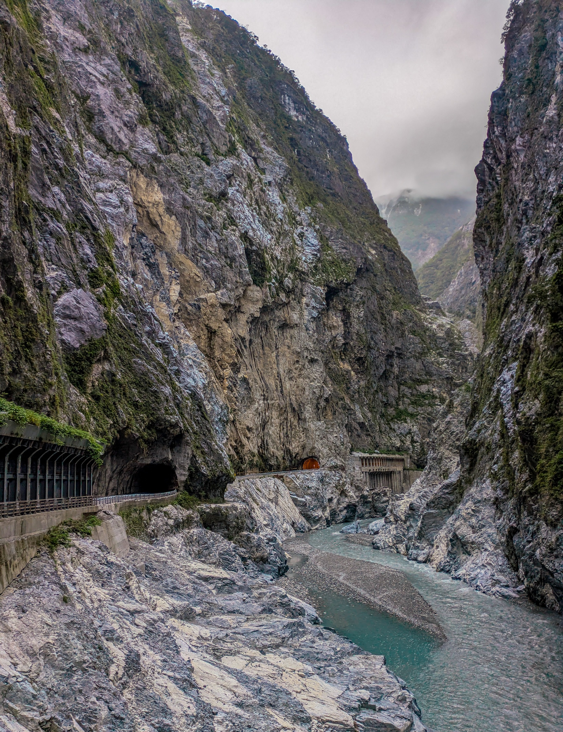 A turquoise river flows through a deep rocky canyon with a road and tunnel along the cliffside.