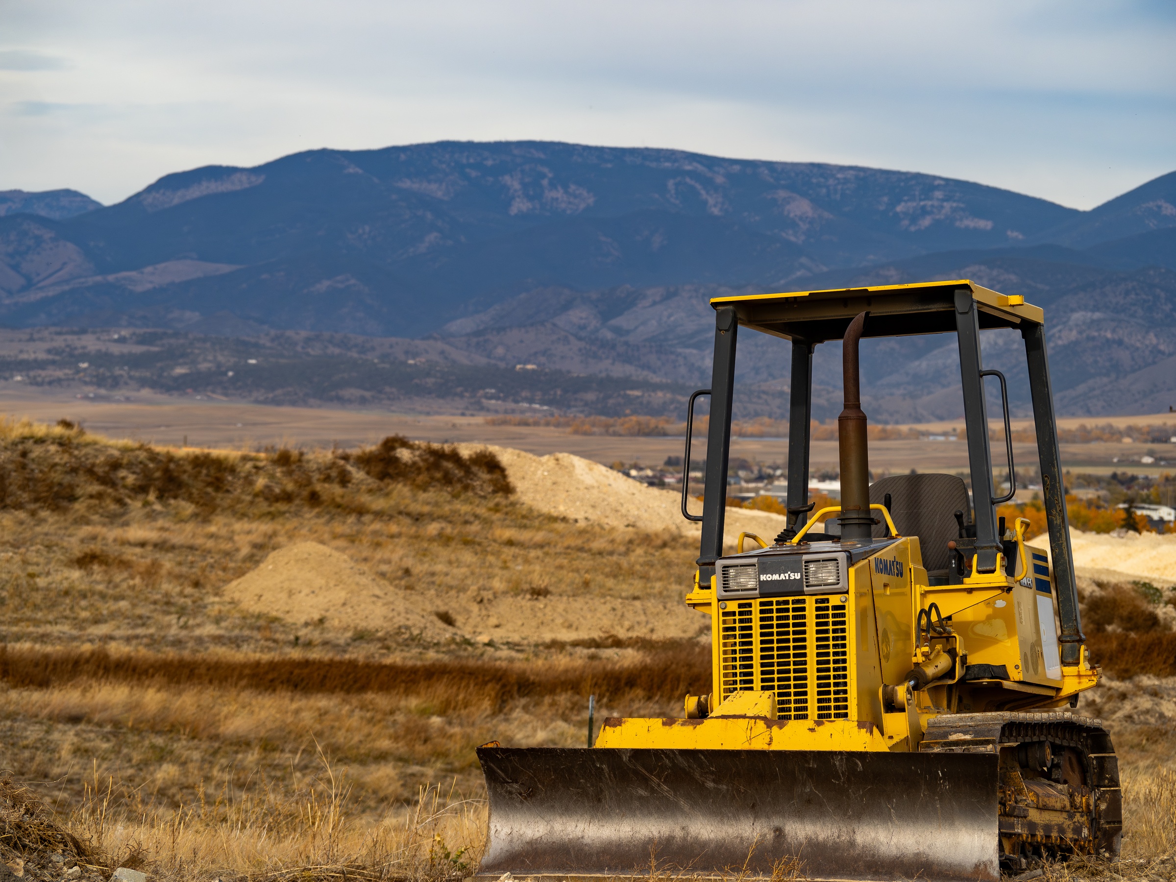 A yellow bulldozer sits in a field with mountains visible in the distance.