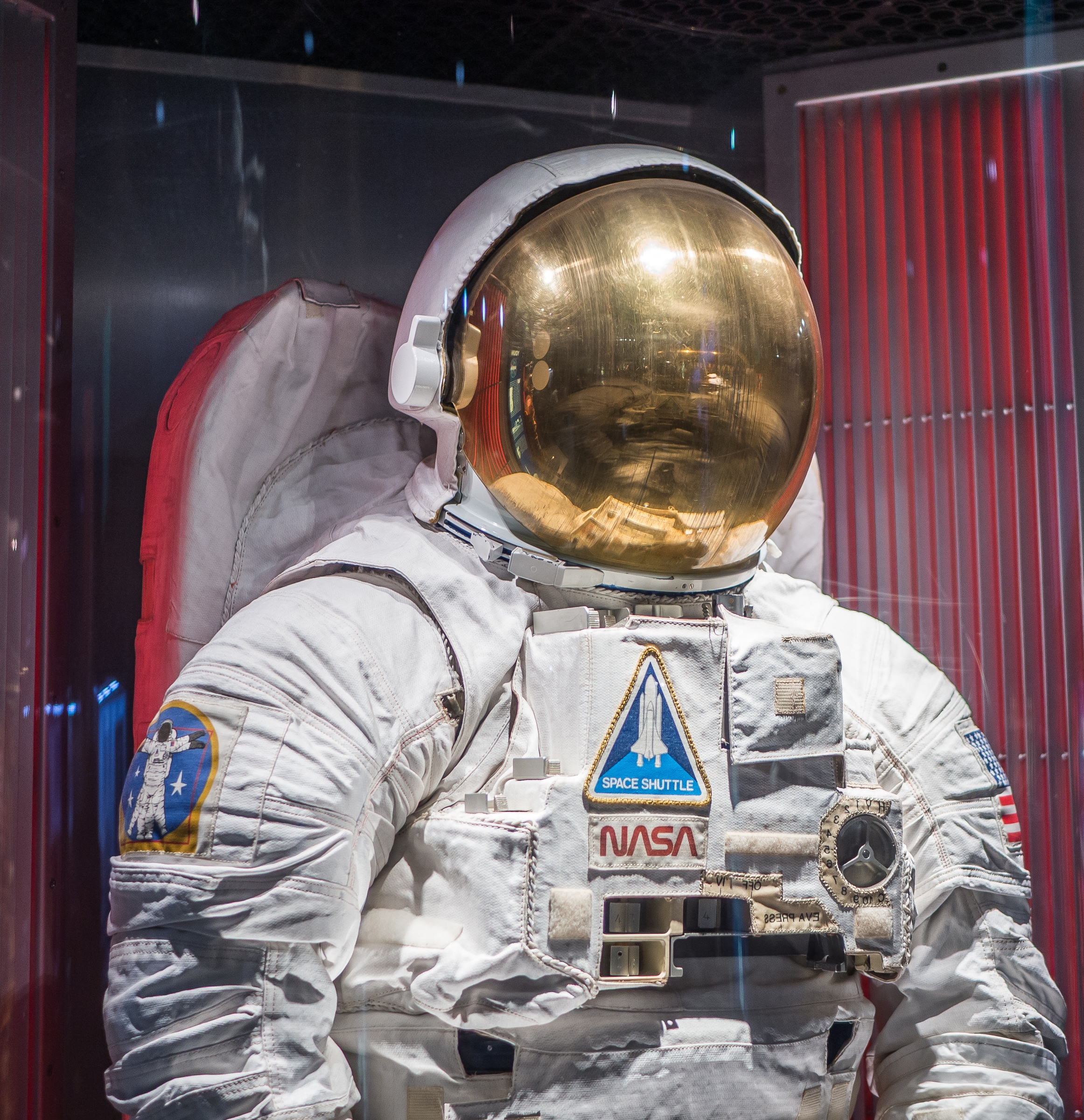A spacesuit with a NASA patch is displayed in a museum setting.