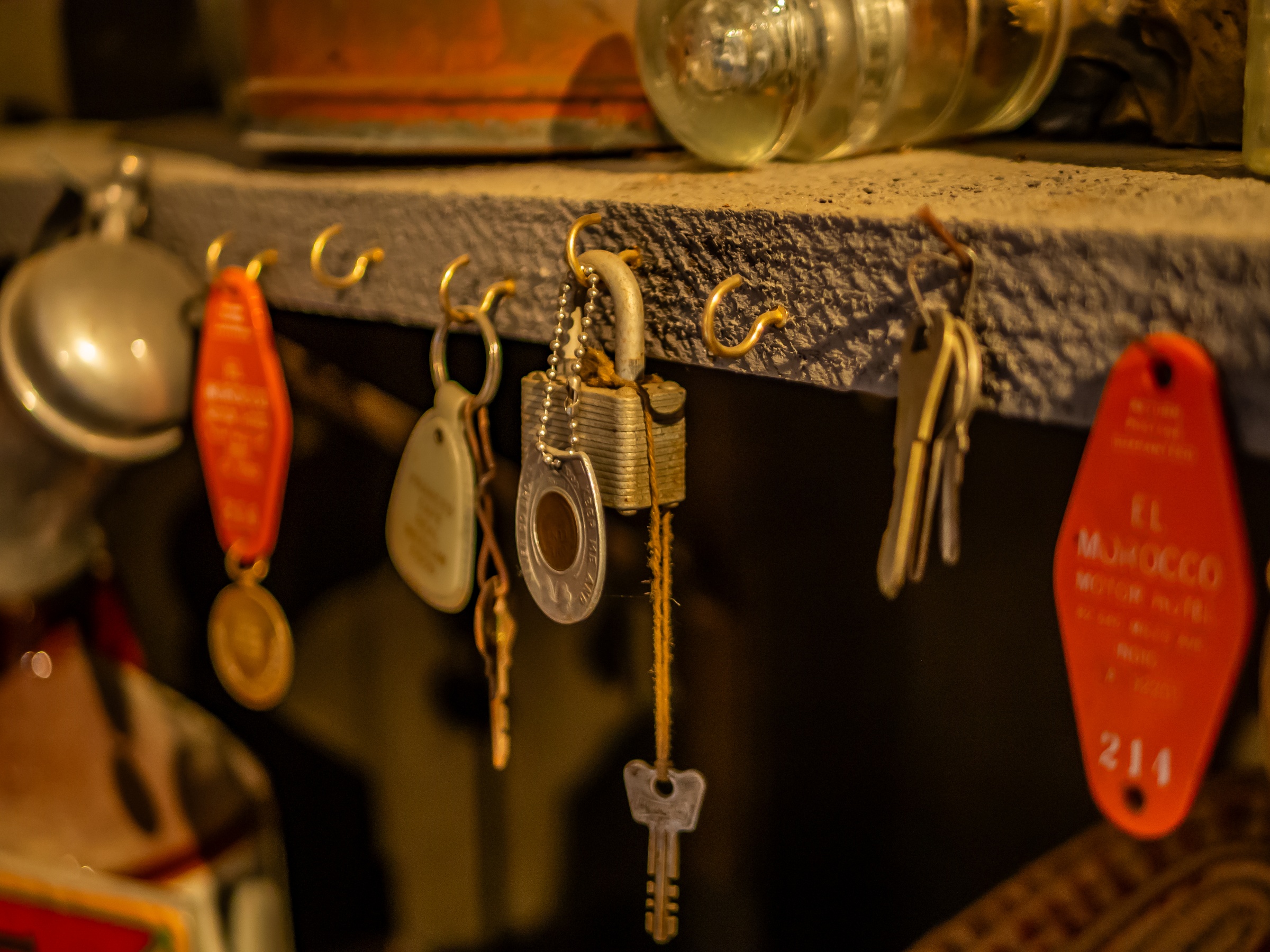 Keys, locks, and keychains hang from a weathered wooden shelf against a dark background.