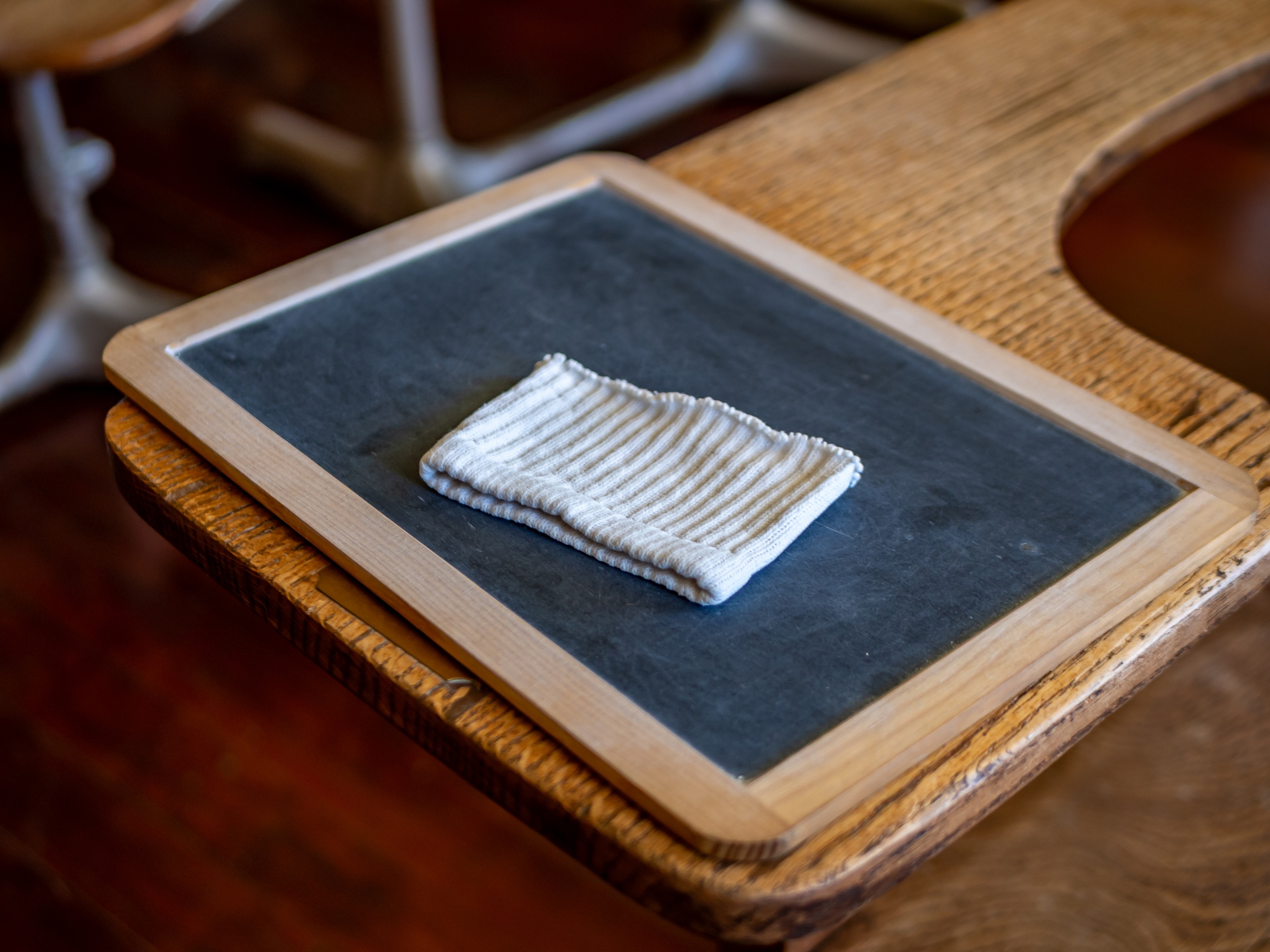 A small white crocheted square rests on a slate board atop a wooden desk.