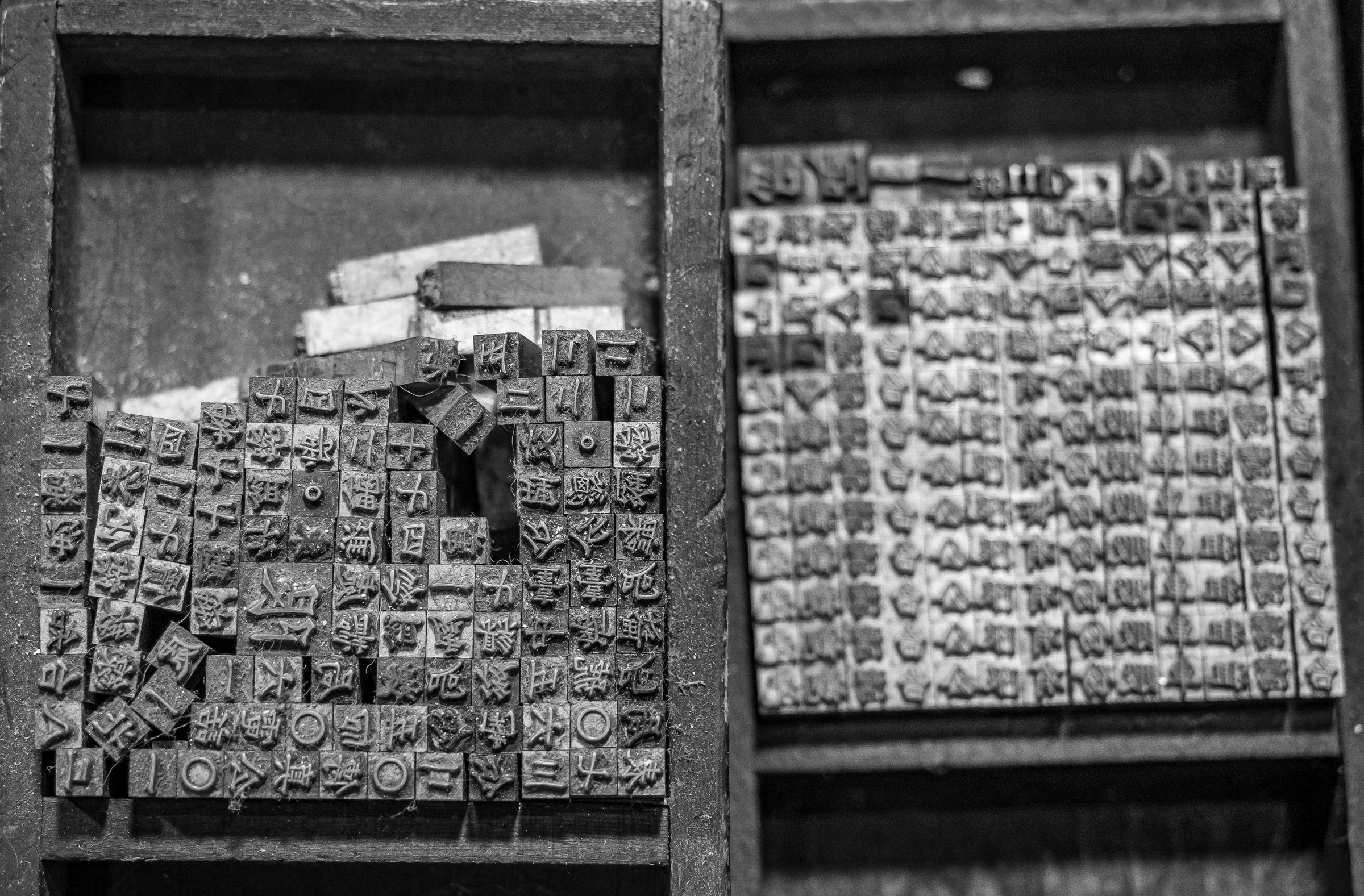 Wooden drawers hold stacks of vintage letterpress type blocks in a black and white photograph.
