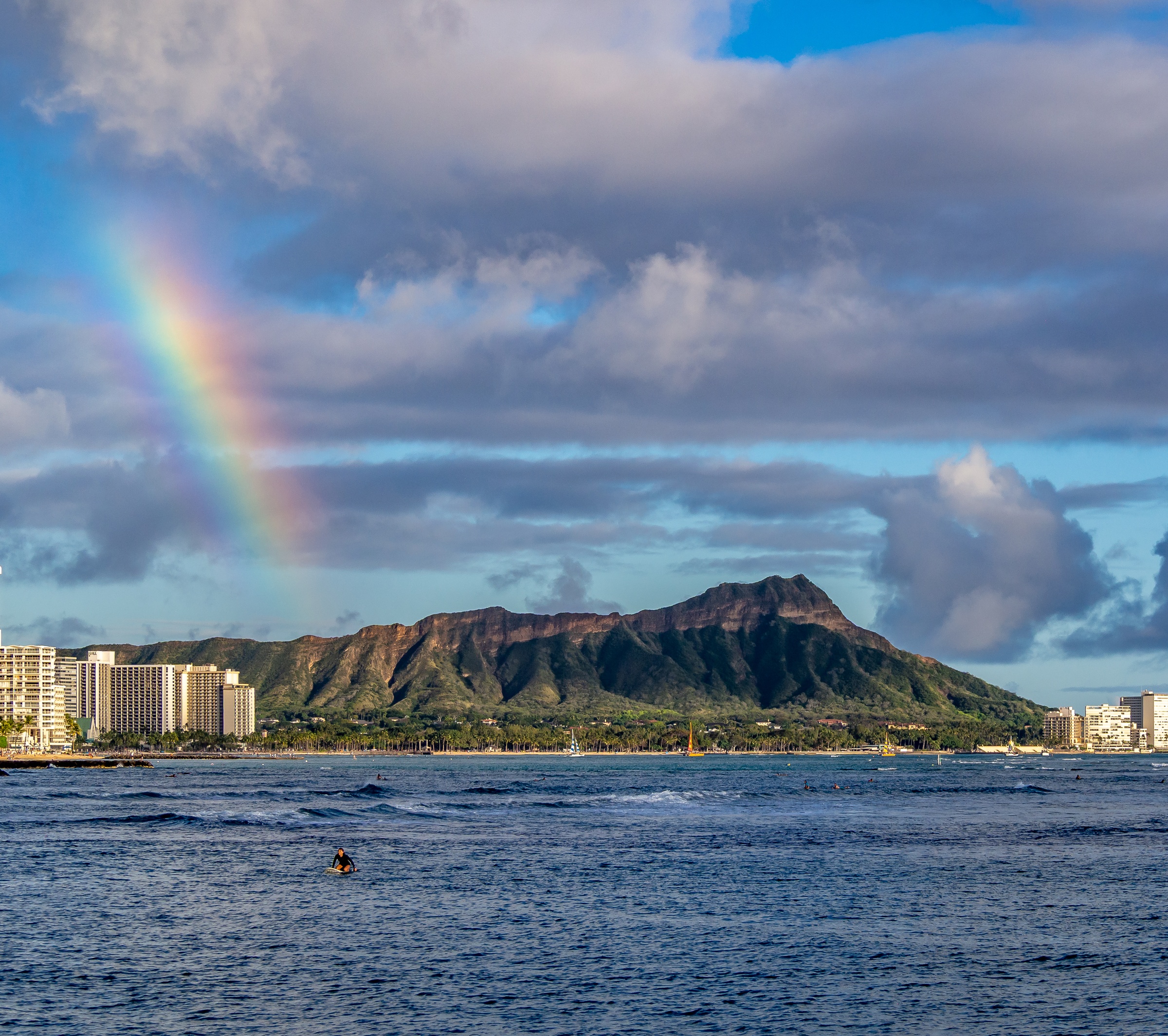 A rainbow arcs over a coastal city and a large mountain beside the ocean.