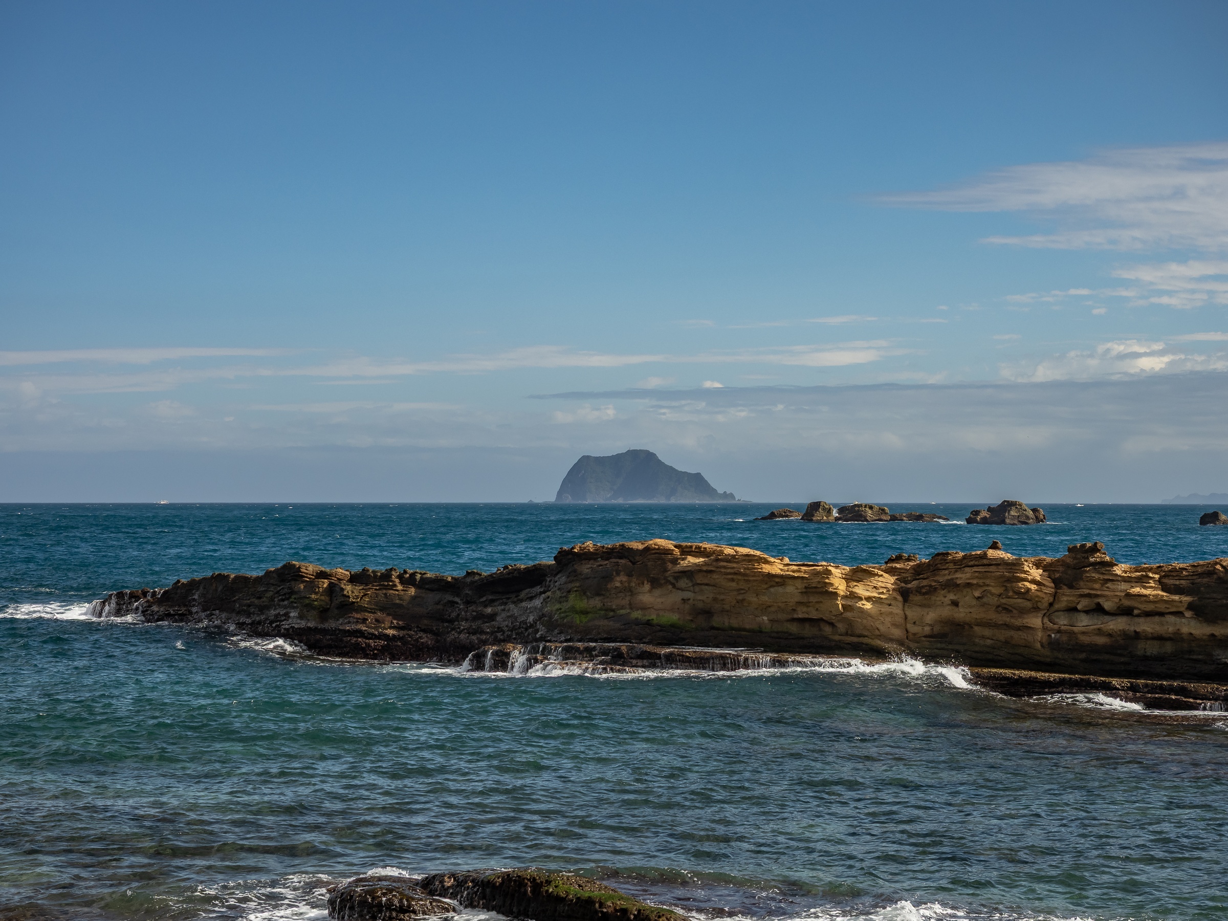 Rocky formations in the blue ocean with a distant island on the horizon.