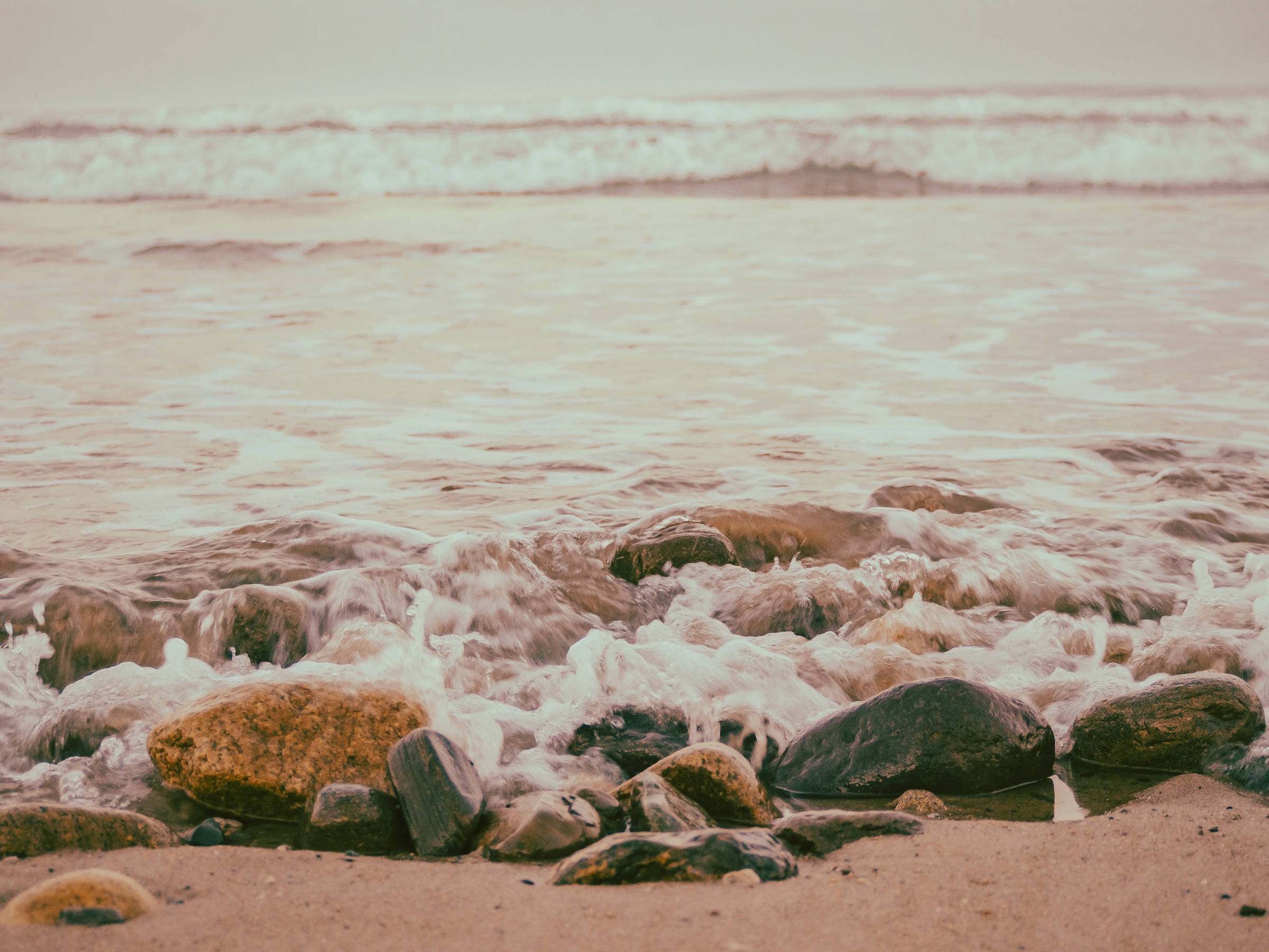 Ocean waves crash over smooth rocks and sand on a beach.
