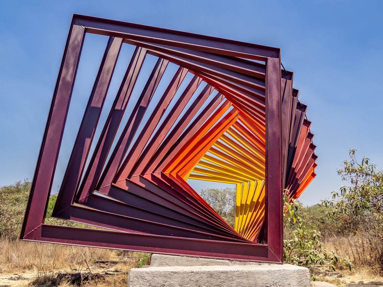 A giant steel square construction painted in a gradient of orange, arcing backward.