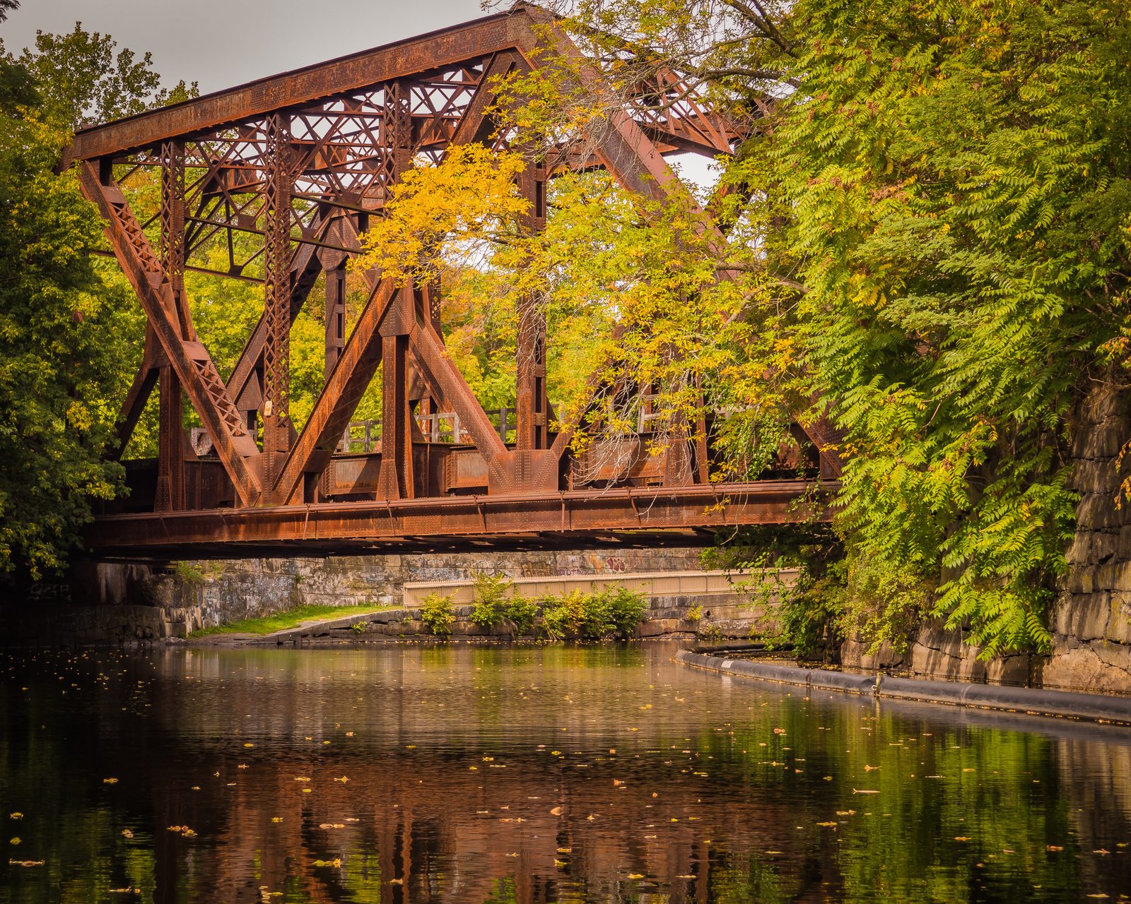 Fall colors on either side of a rusty train truss over a canal.
