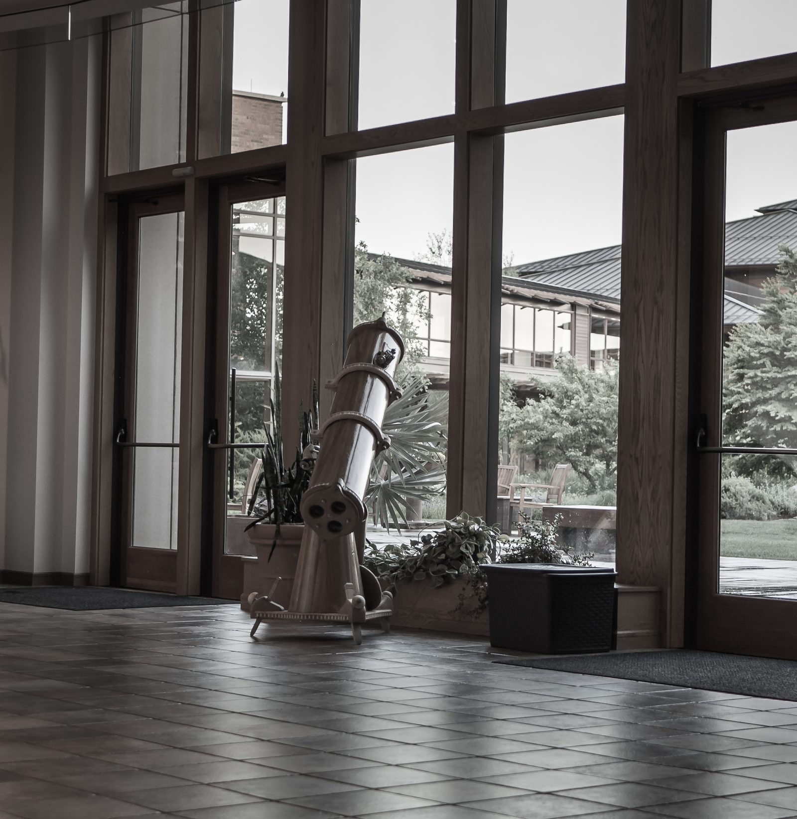 A telescope faces out a window in a fancy office building foyer.